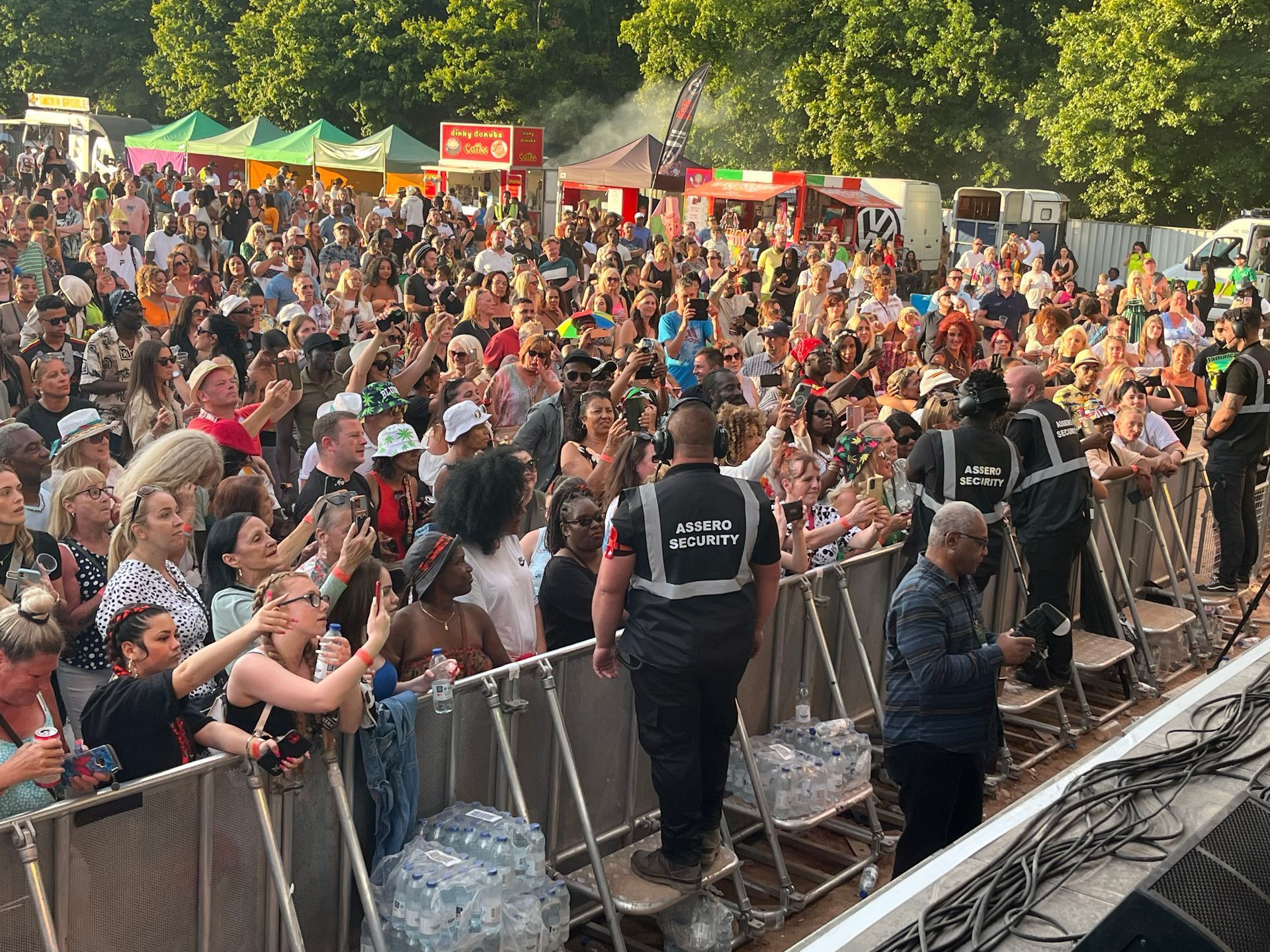 Large crowd at an outdoor concert, with security personnel and food stalls visible.