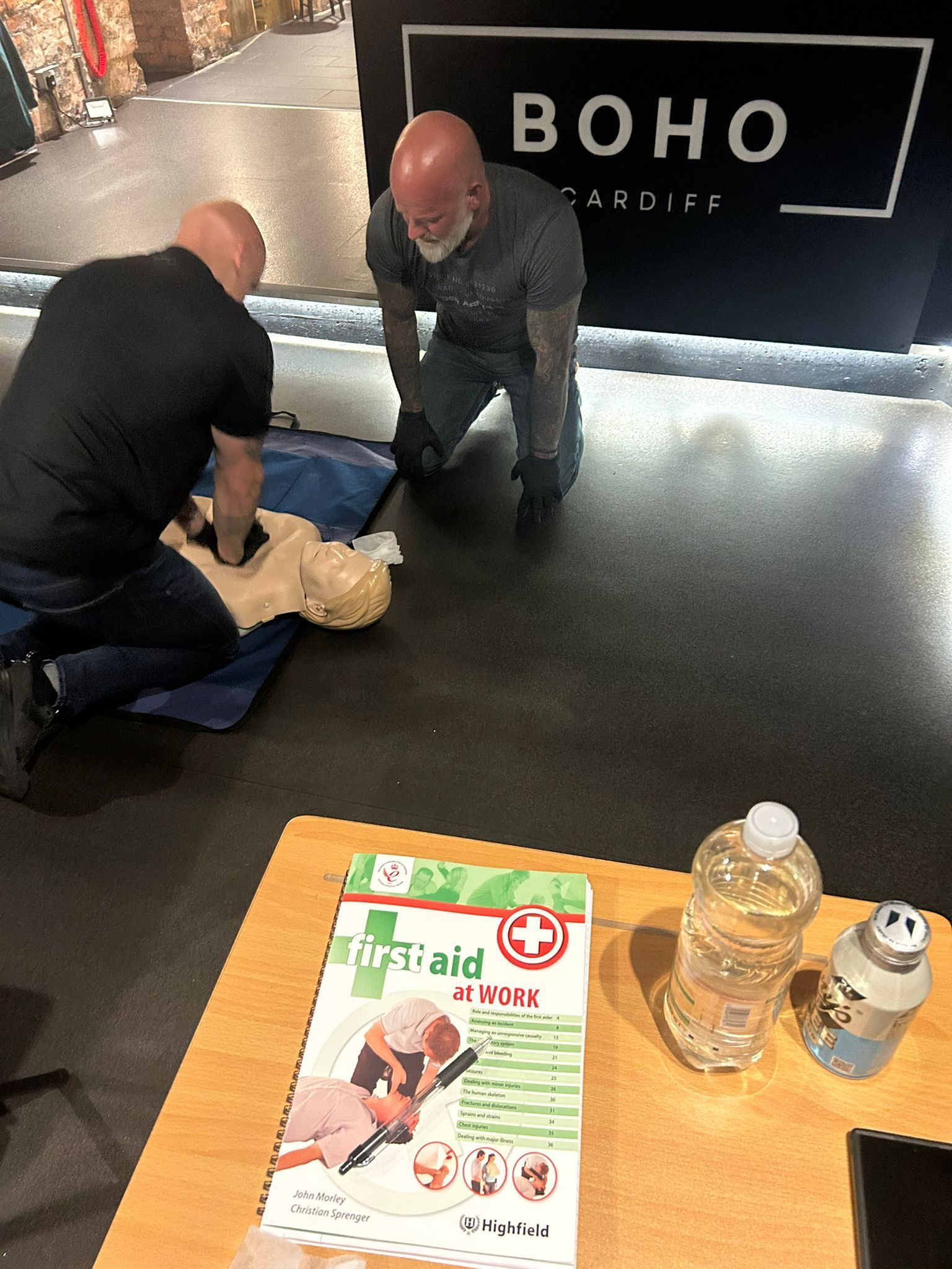 Two men are practicing first aid on a mannequin.