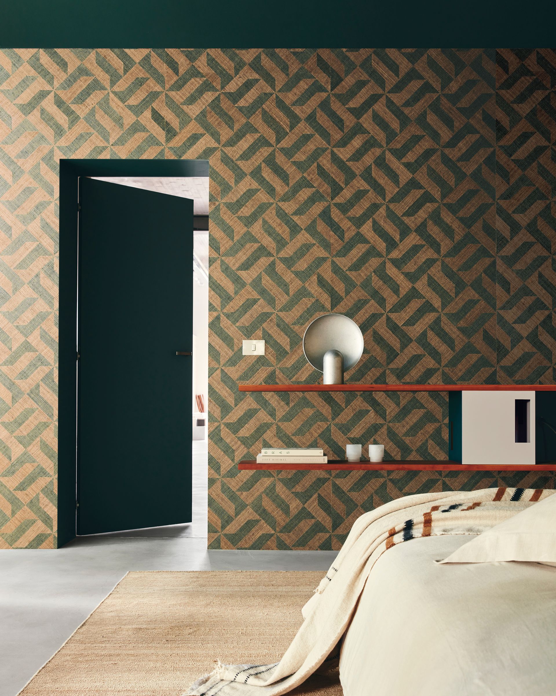 Camera da letto con parete decorata, porta verde scuro, mensole arancioni con decorazioni e un letto con una coperta color crema.