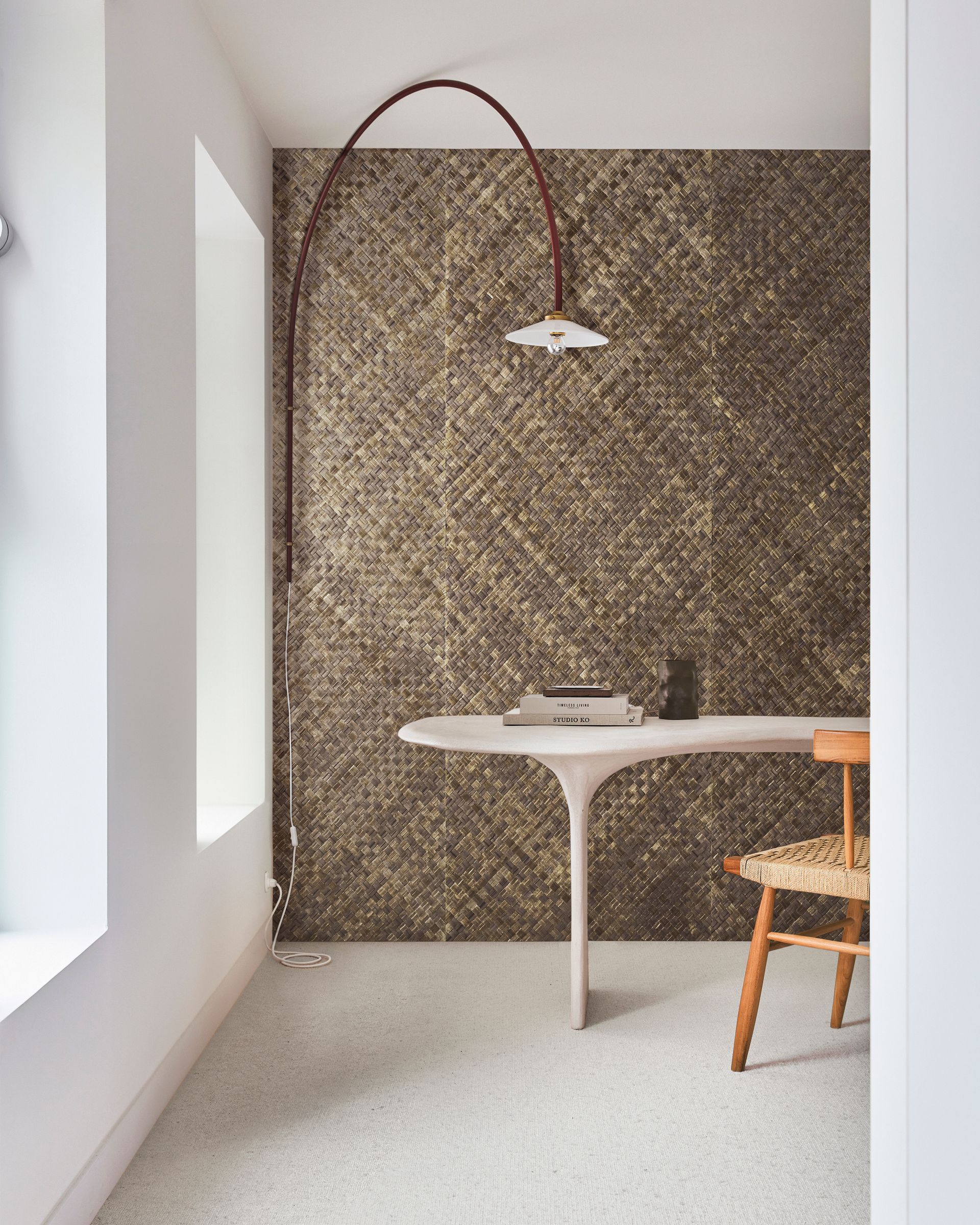 Piccola stanza con scrivania, sedia e lampada ad arco contro una parete dorata testurizzata.