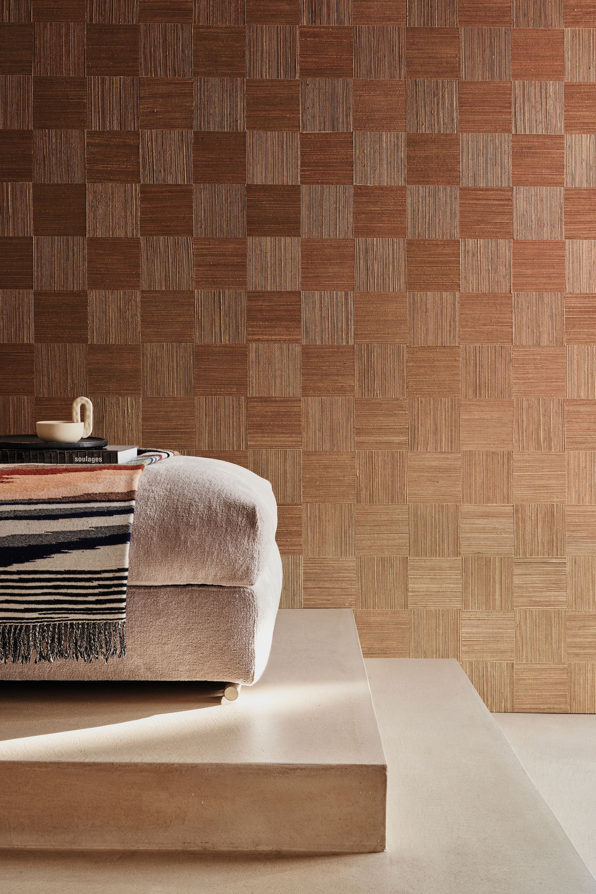 Parete in tessuto marrone testurizzato dietro un divano dai toni neutri su una piattaforma.