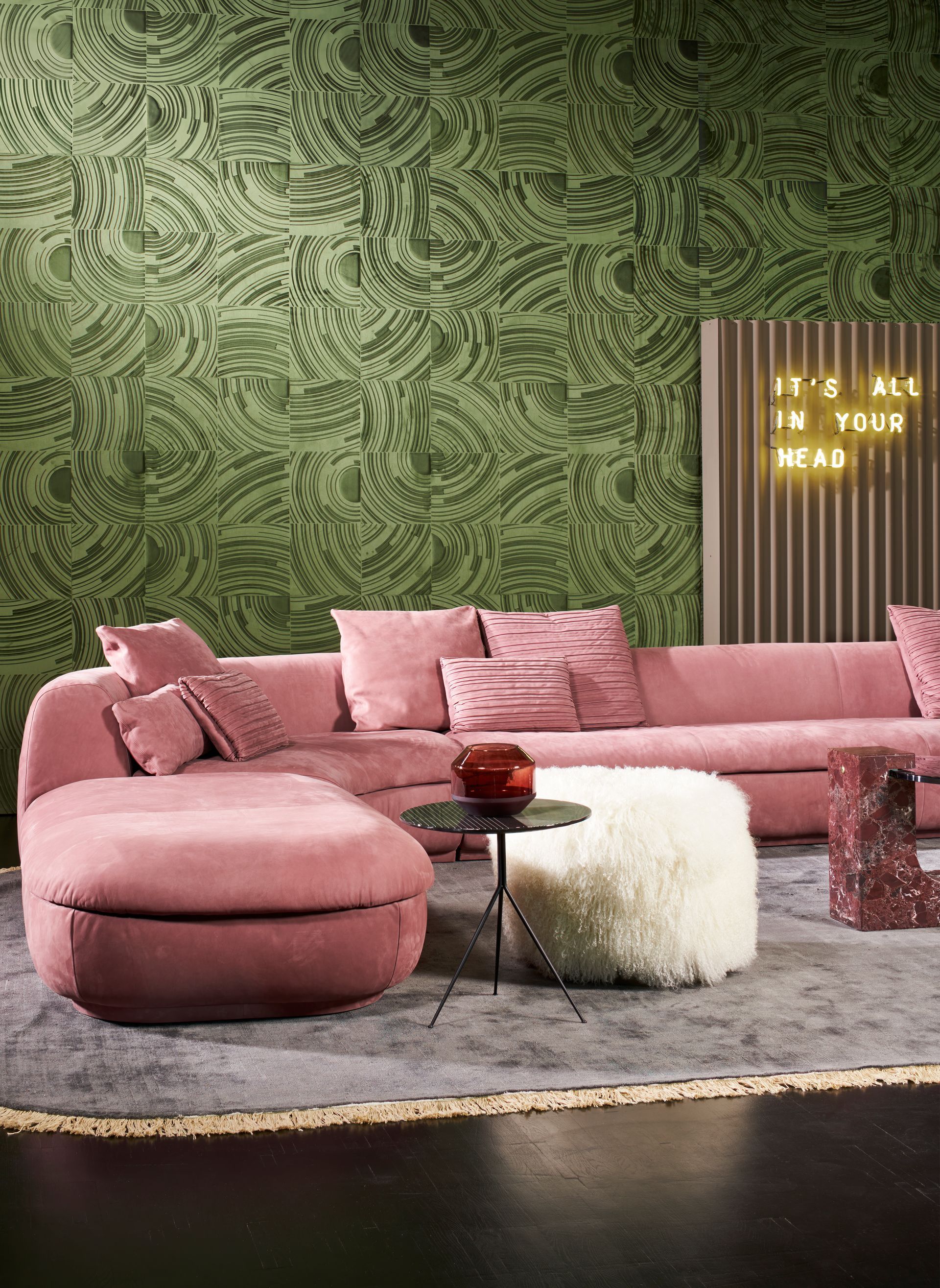 Divano componibile rosa in un soggiorno con carta da parati a motivi verdi e insegna al neon.