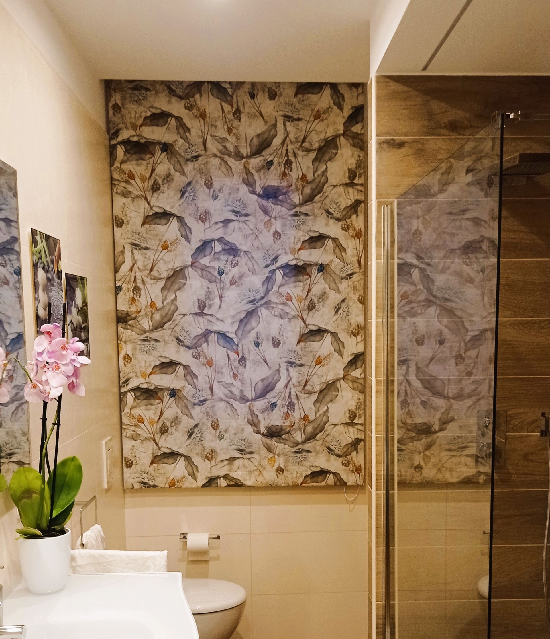 Bagno con parete decorativa decorata, sanitari bianchi, orchidea e porta della doccia in vetro.