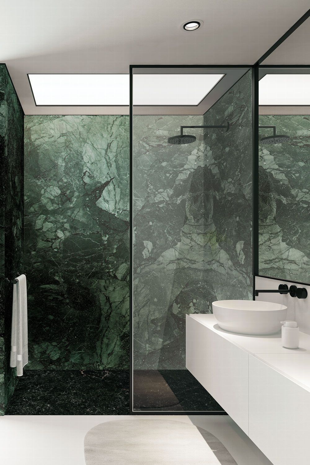 Bagno moderno con pareti in marmo verde, doccia in vetro con cornice nera, lavandino bianco e lucernario sopraelevato.