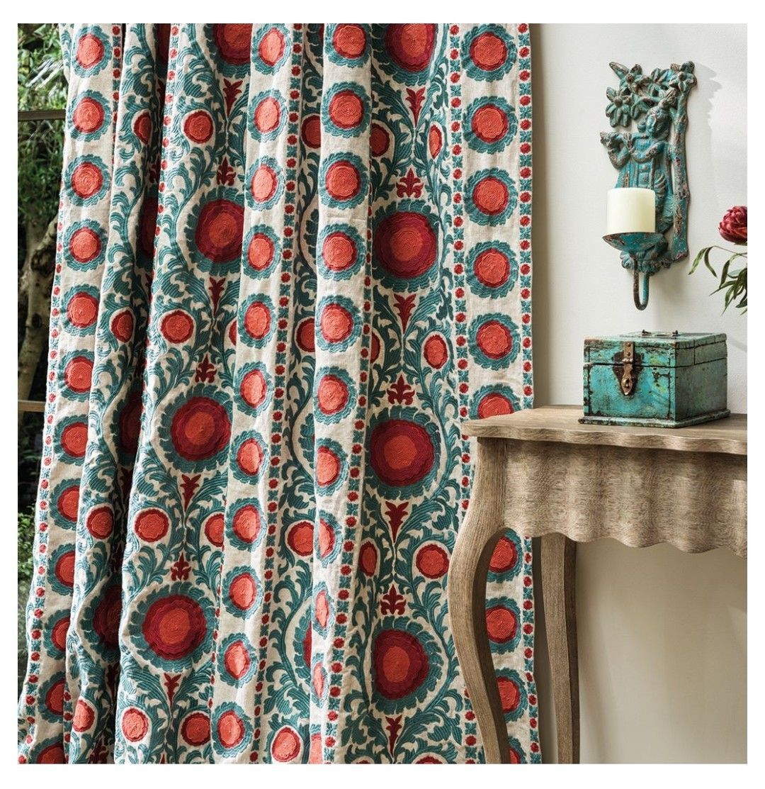 Tende con motivi floreali rossi e verde acqua, accanto a un tavolo con un'applique e una piccola cassettiera verde acqua.