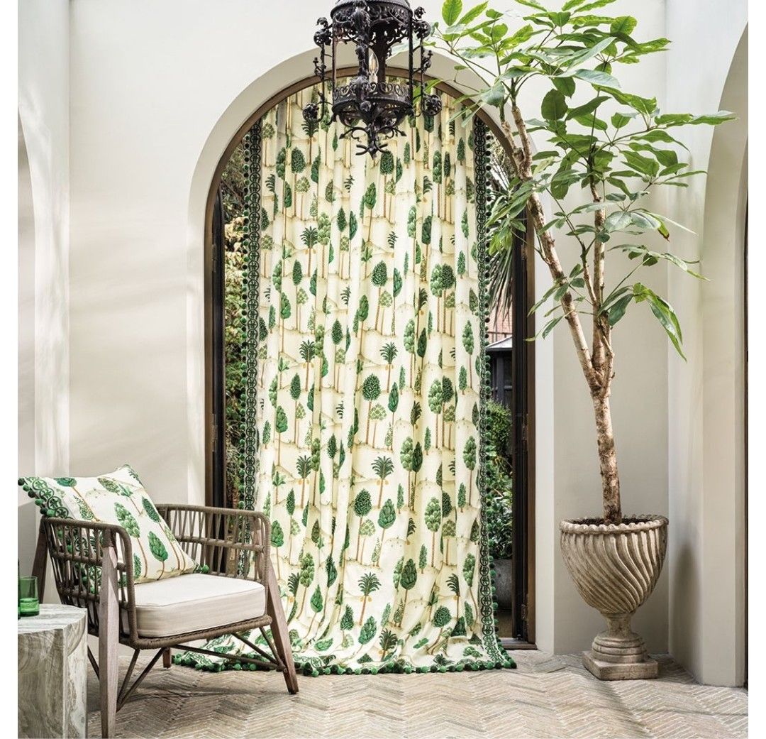 Patio esterno con sedia, tende con motivi di alberi verdi e pianta in vaso.