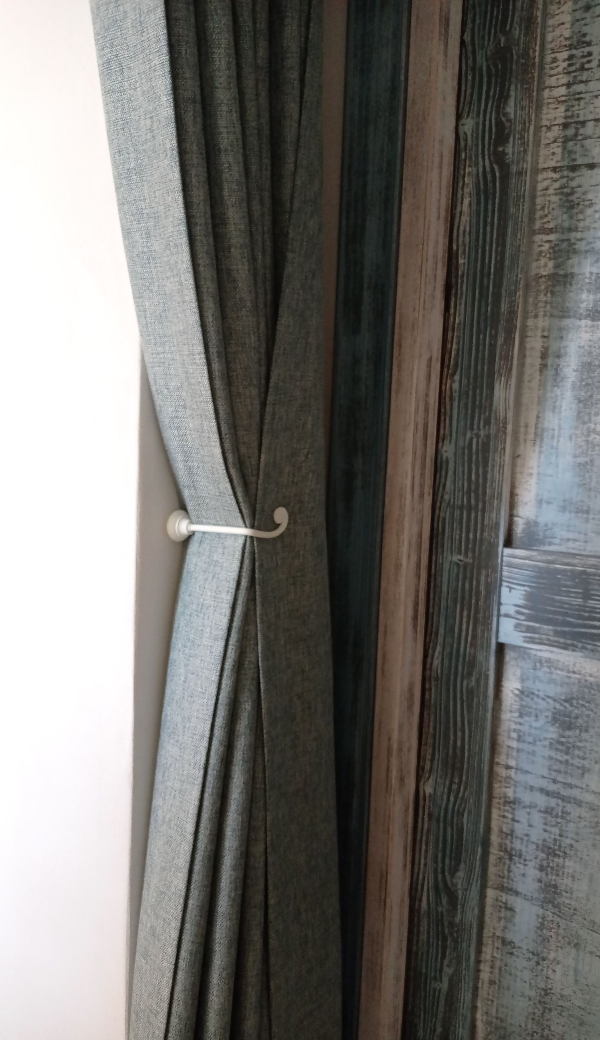 Tende grigie appese a un gancio argentato, accanto a una porta grigio-blu consumata dal tempo.