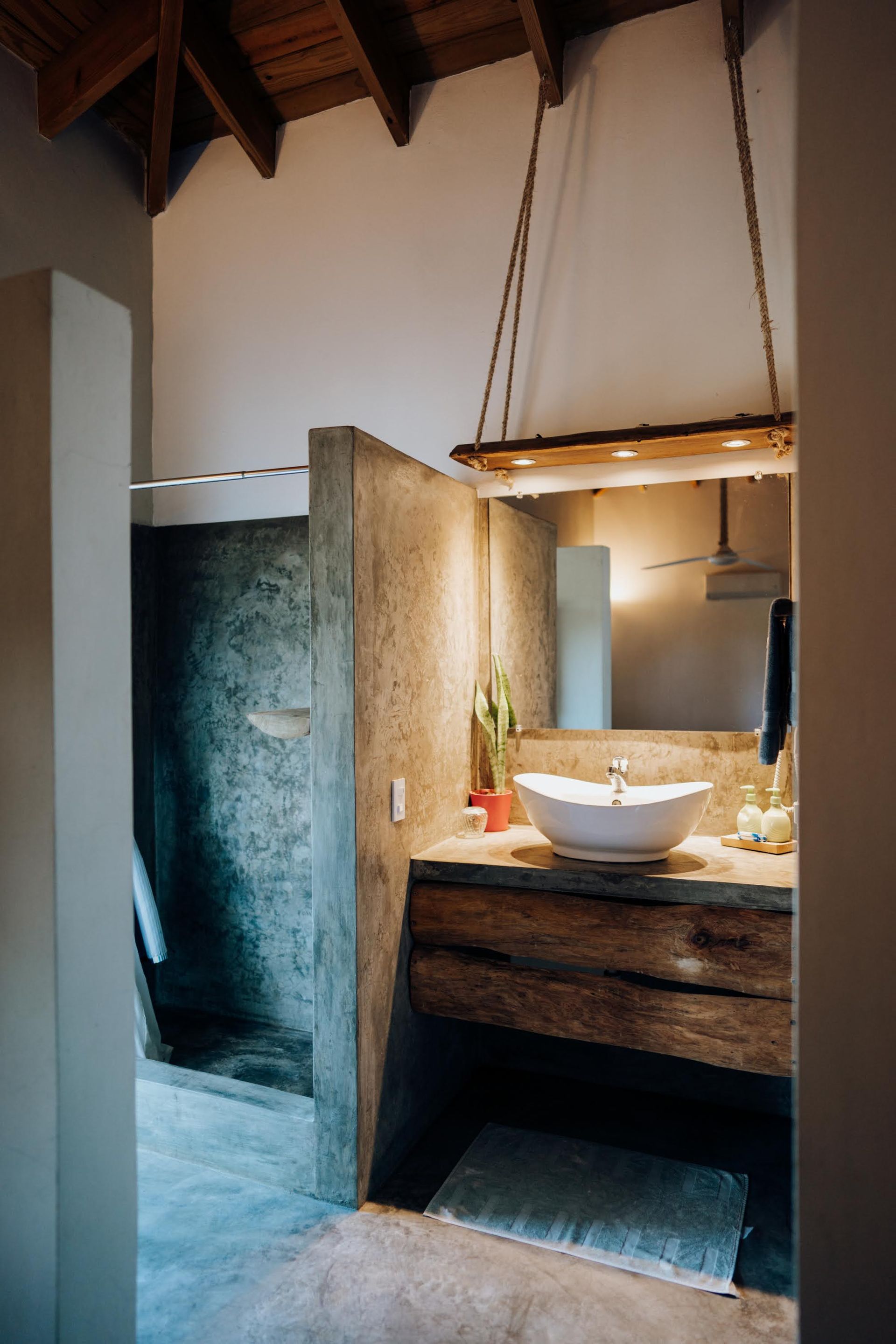 Rustic bathroom with concrete shower, wooden vanity, and hanging mirror.