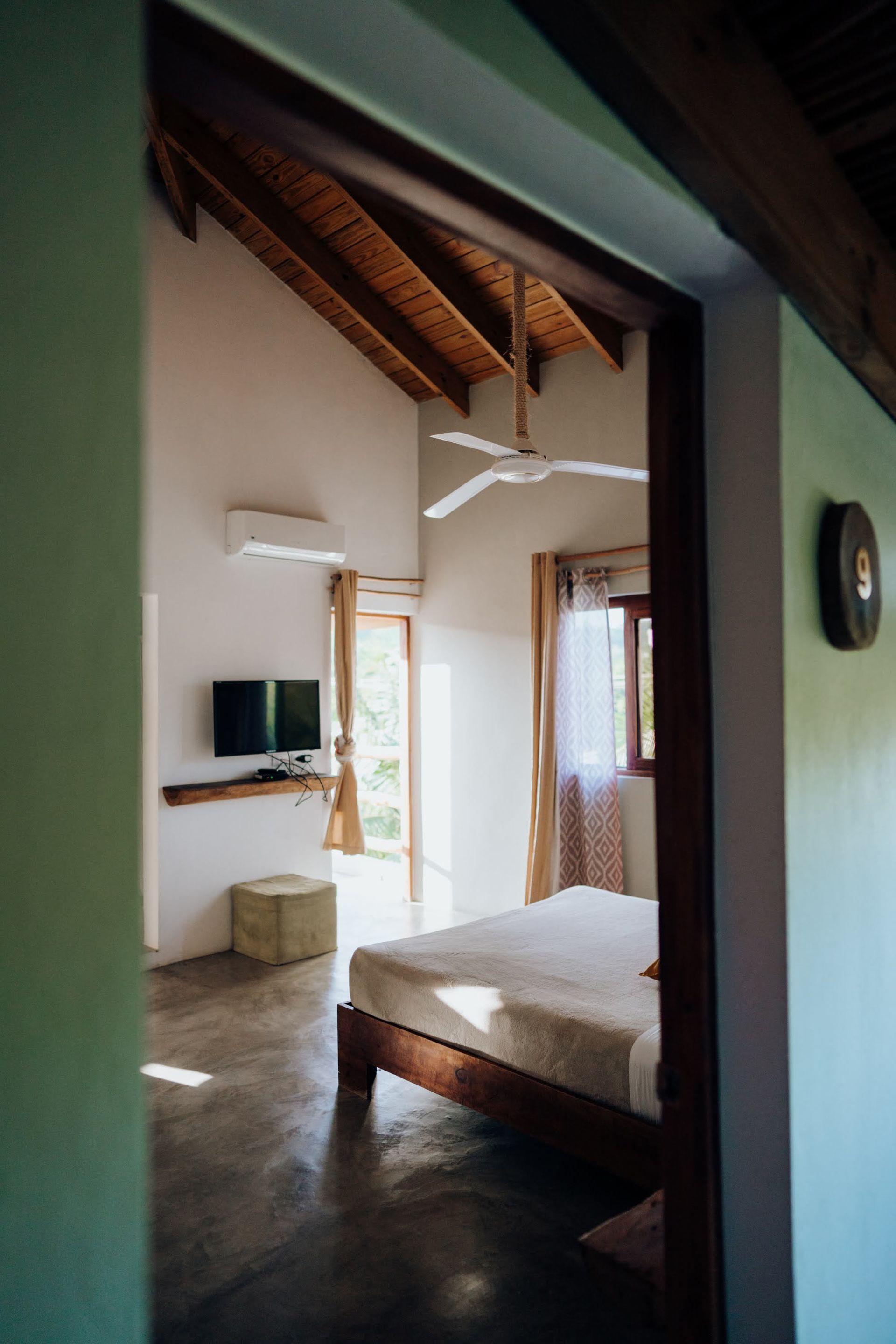 Bedroom interior with bed, TV, ceiling fan, and open door to outside.