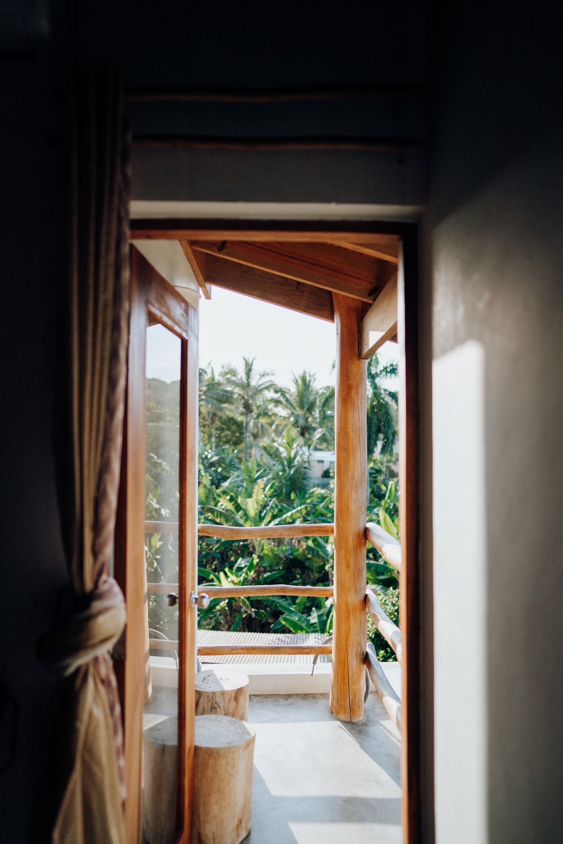 Balcony overlooking lush green trees, framed by a wooden door and curtain.