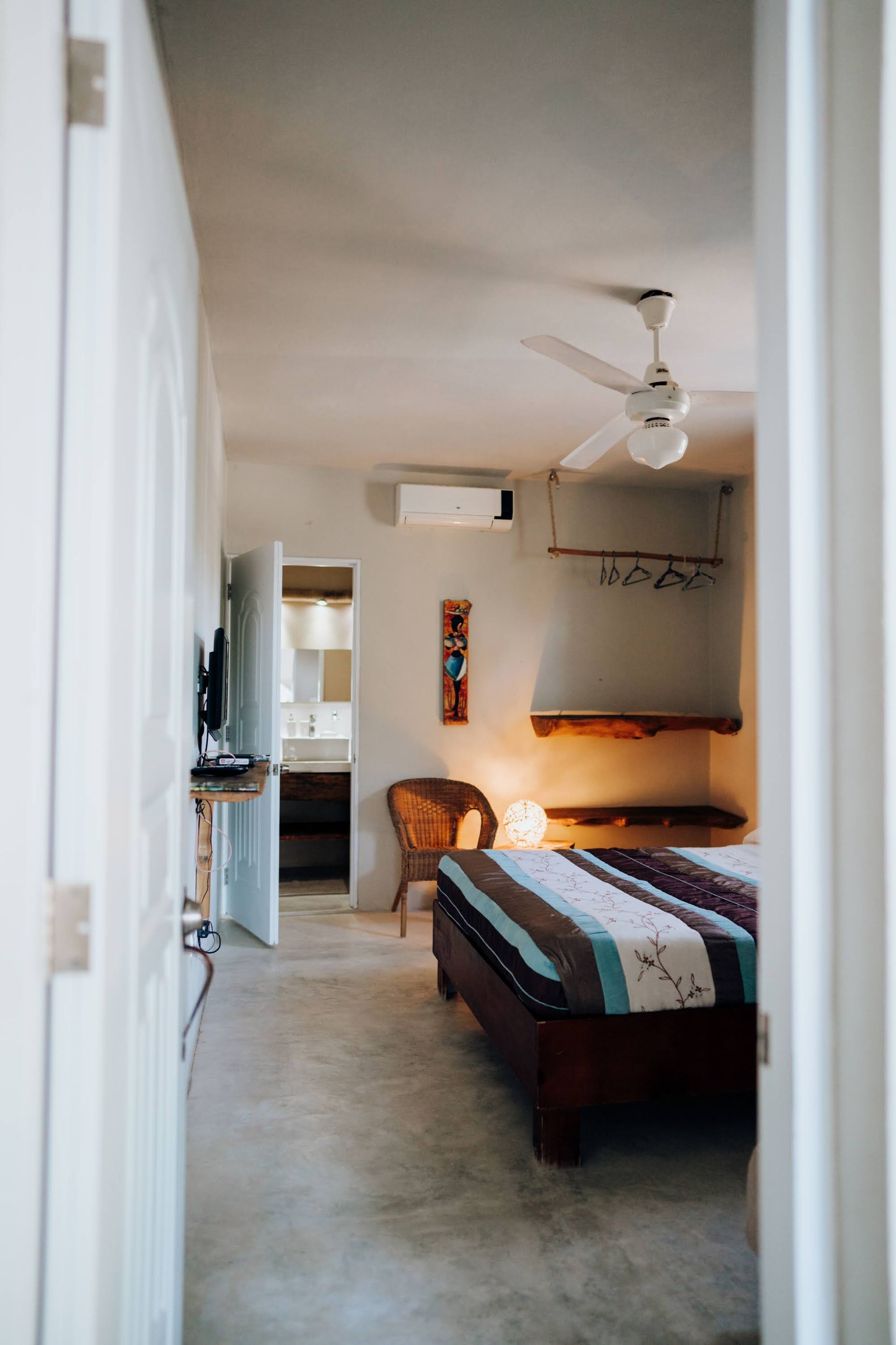 Bedroom interior, bed with striped blanket, open door to bathroom, chair.