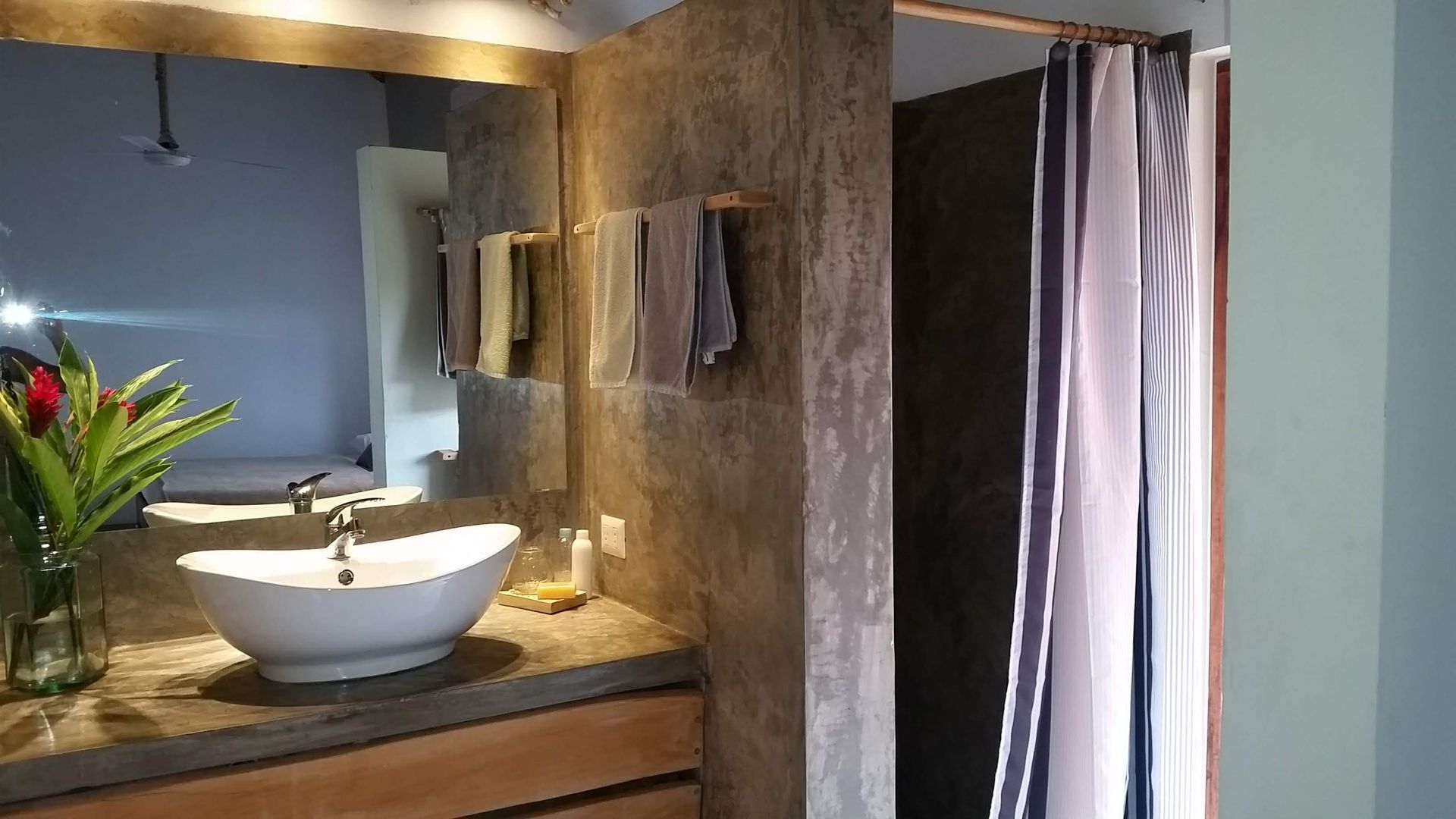 Bathroom with a white sink, mirror, concrete walls, towels, and shower curtain.