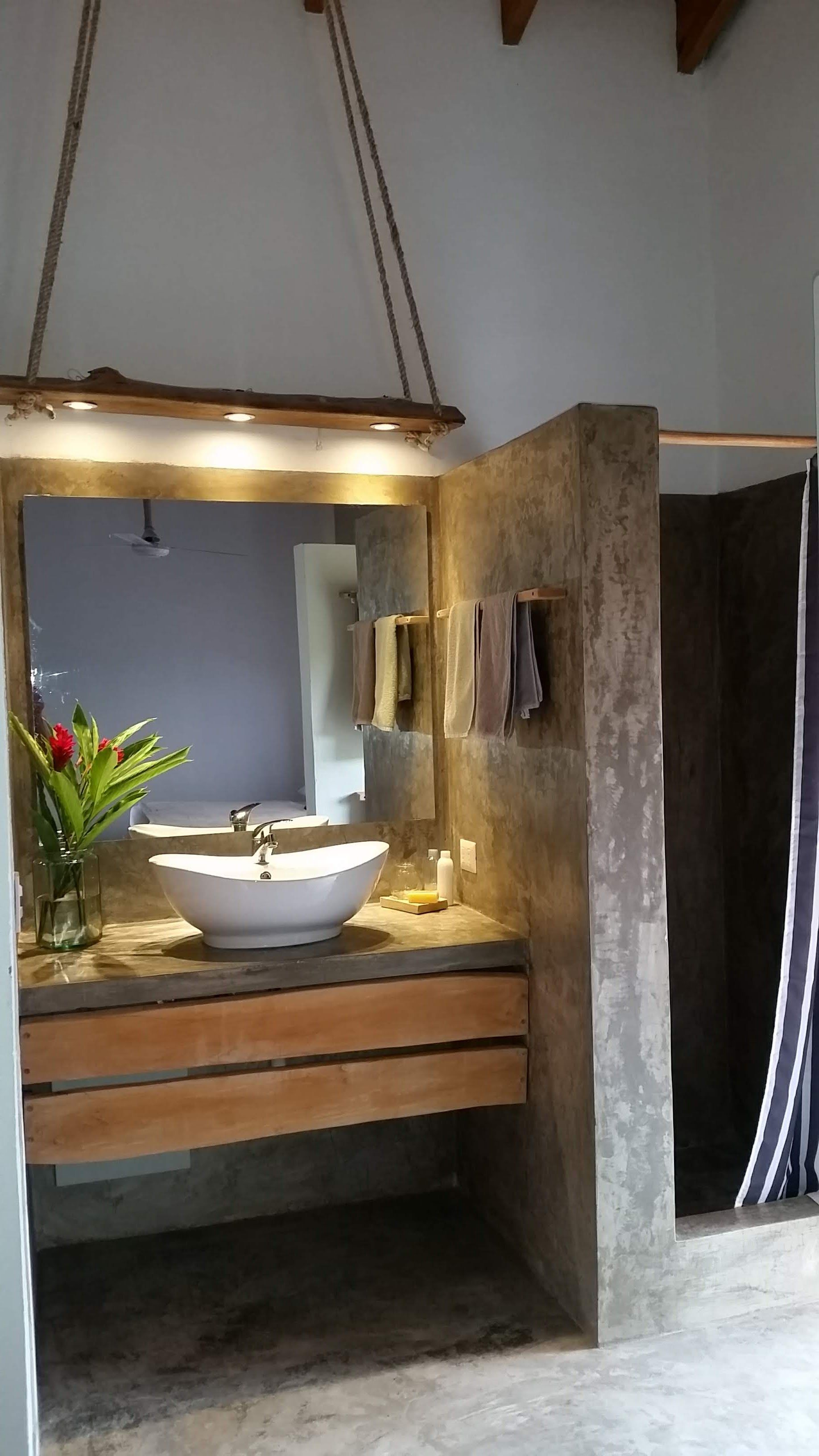 Bathroom with concrete walls, wooden cabinets, vessel sink, and shower stall.