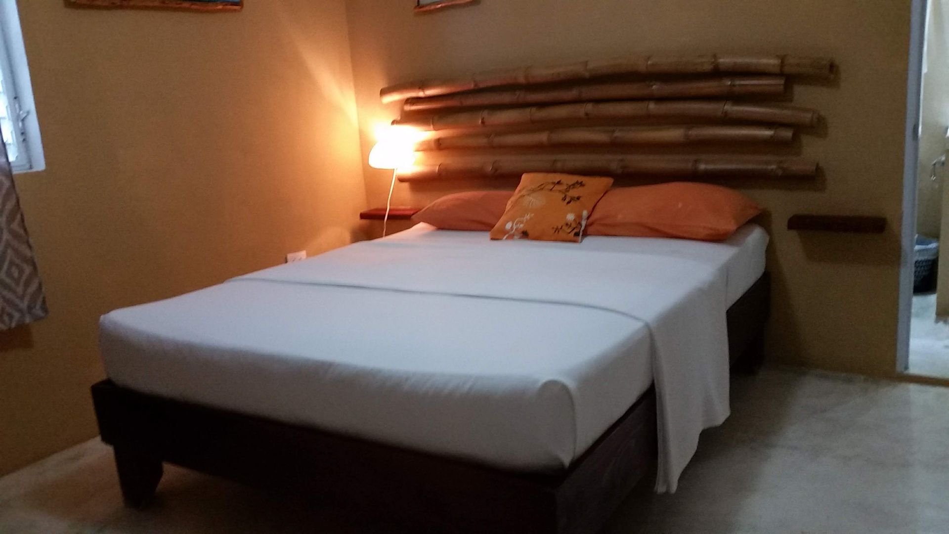 Bedroom with a bed, bamboo headboard, and orange accents; warm lighting.