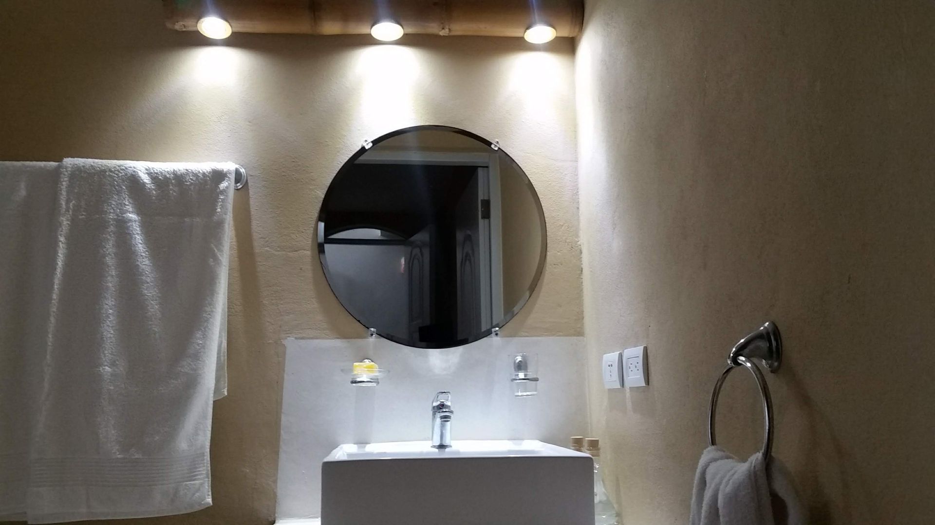 Bathroom with a round mirror above a white sink, towel rack, and lights.