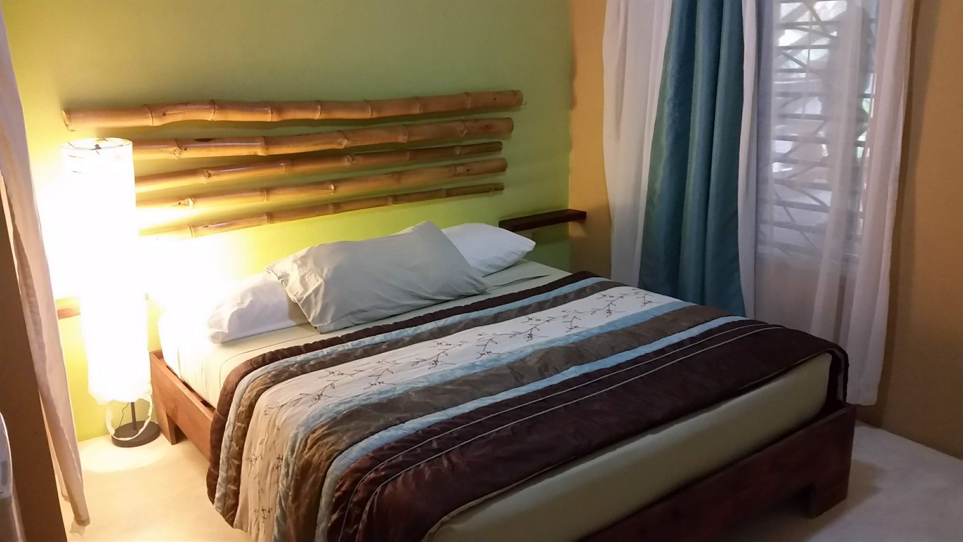 Bedroom with bed, bamboo headboard, bedside lamp, and teal curtains.