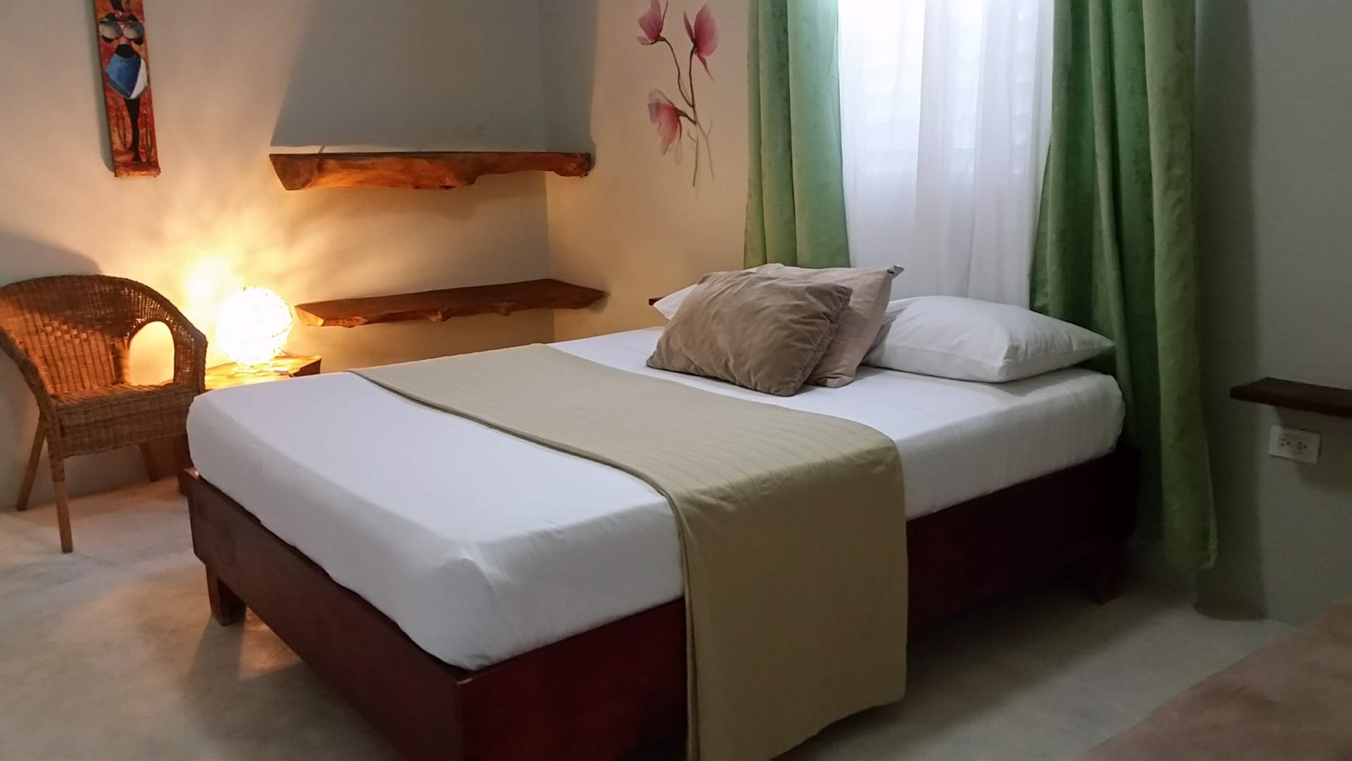 Bedroom with bed, wicker chair, shelves, green curtains, and floral wall art.