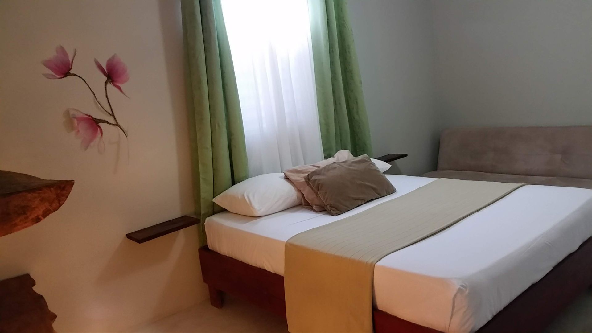 Bedroom with bed, sofa, and window with green curtains. Pink floral wall decor.