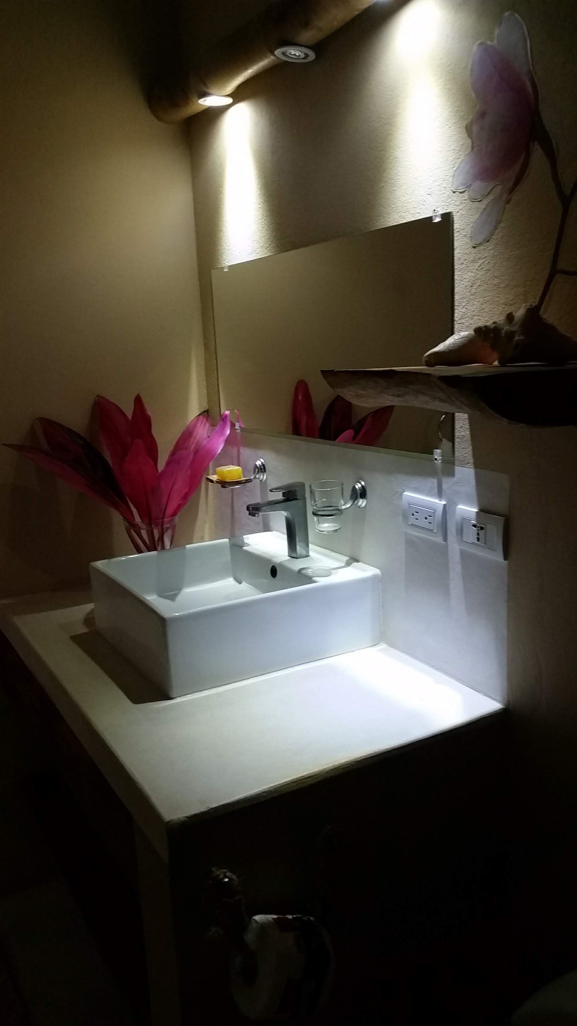 Modern bathroom sink with a white rectangular basin, mirrored backsplash, and decorative pink leaves.