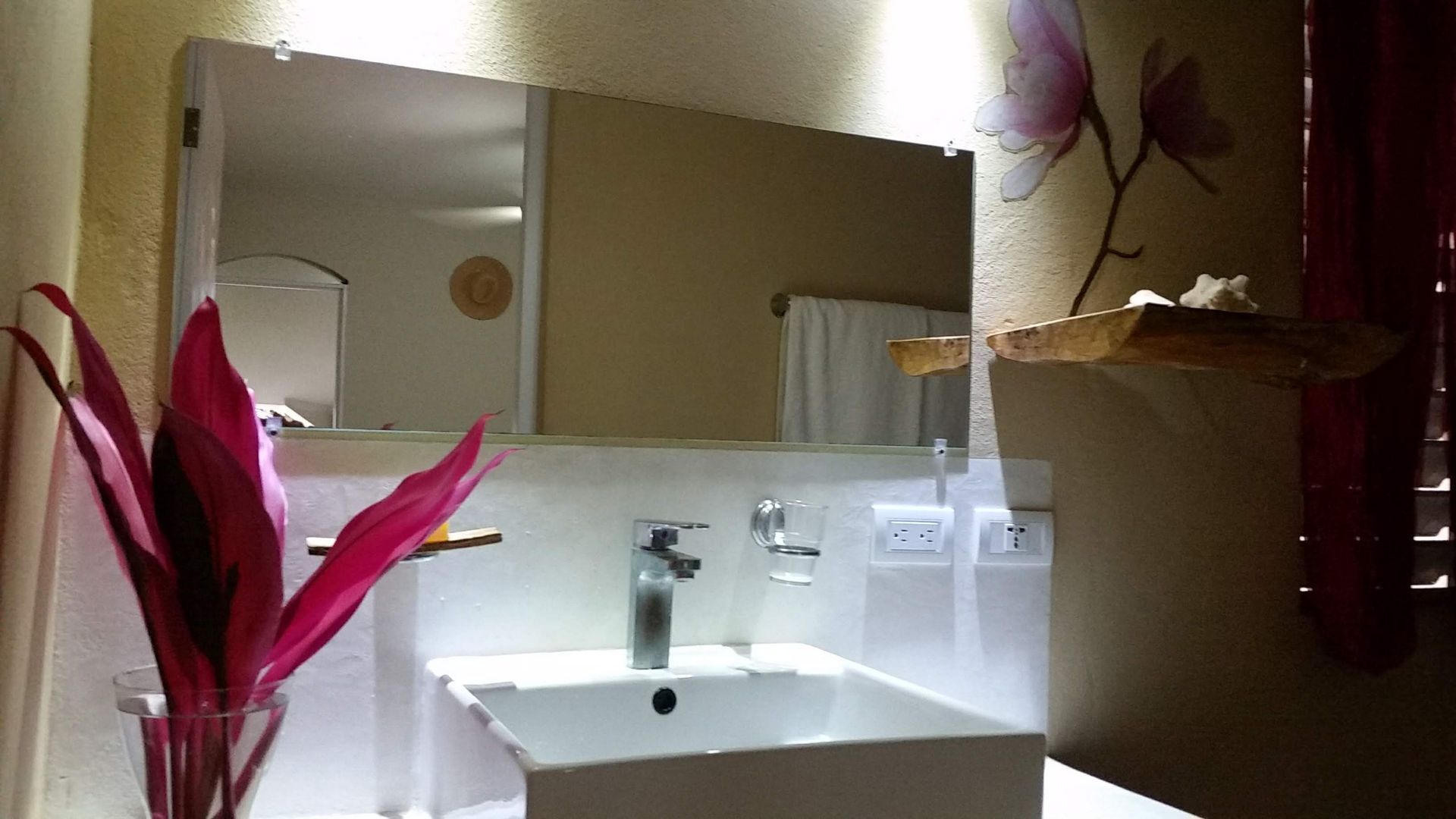 Bathroom with a rectangular mirror above a white sink, red flowers, and floral wall art.