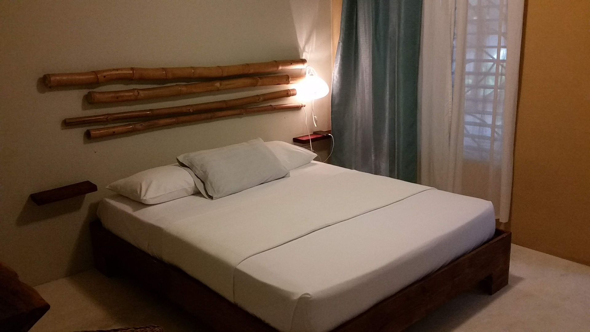 Bedroom with wooden bed frame and headboard made of horizontal branches. White bedding, neutral walls.