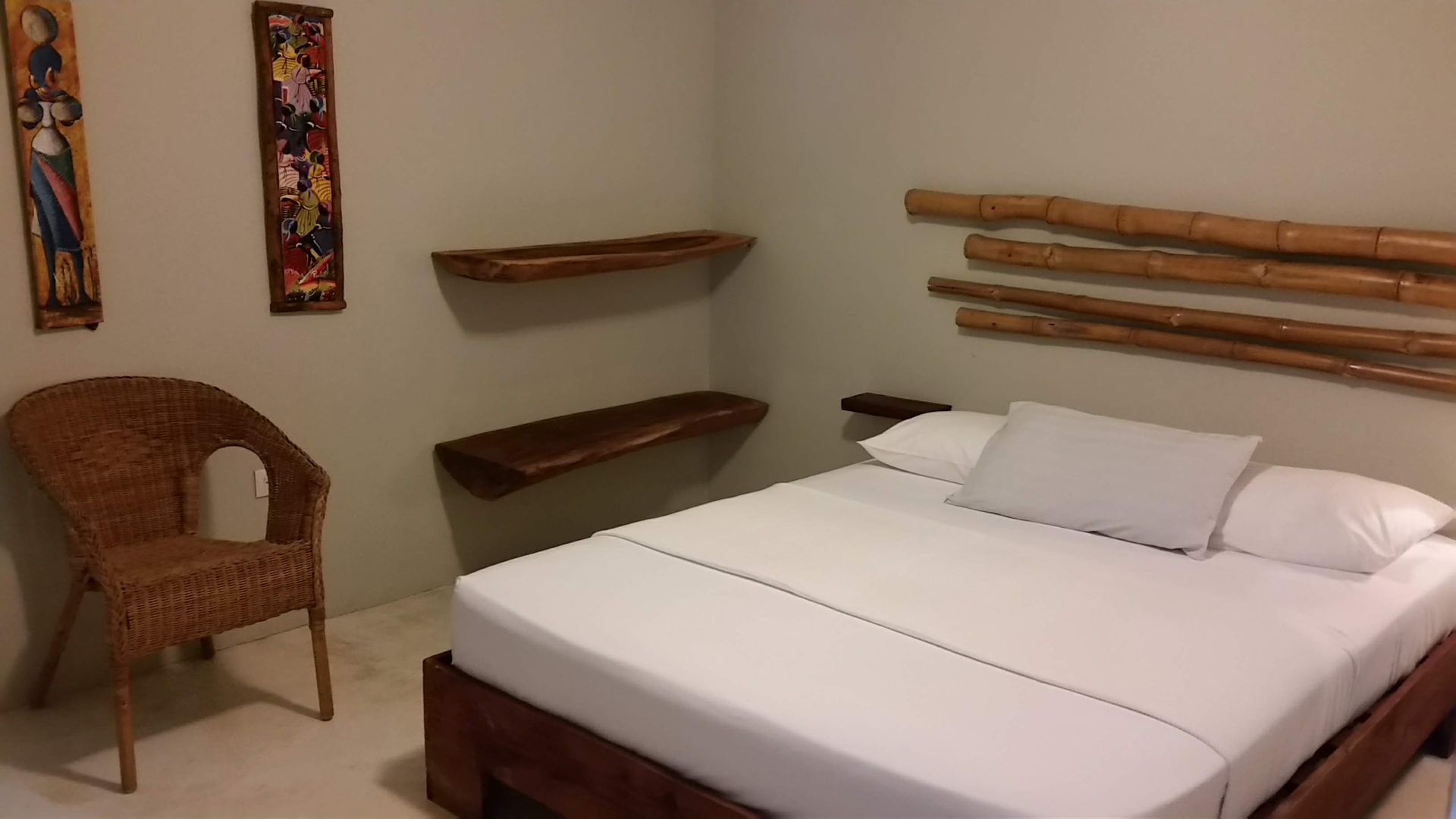 Bedroom with a bed, wicker chair, wooden shelves, and wall art.