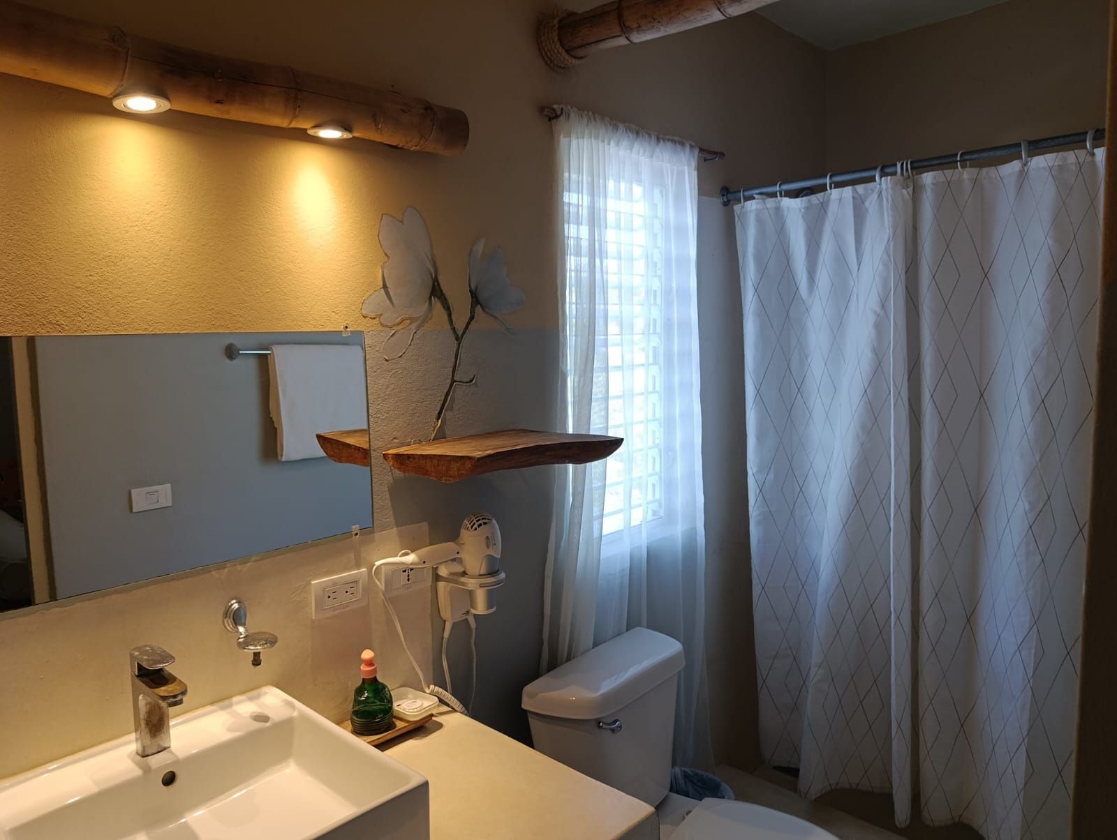 Bathroom with a square sink, toilet, shower curtain, and a window. Beige walls and wooden accents.