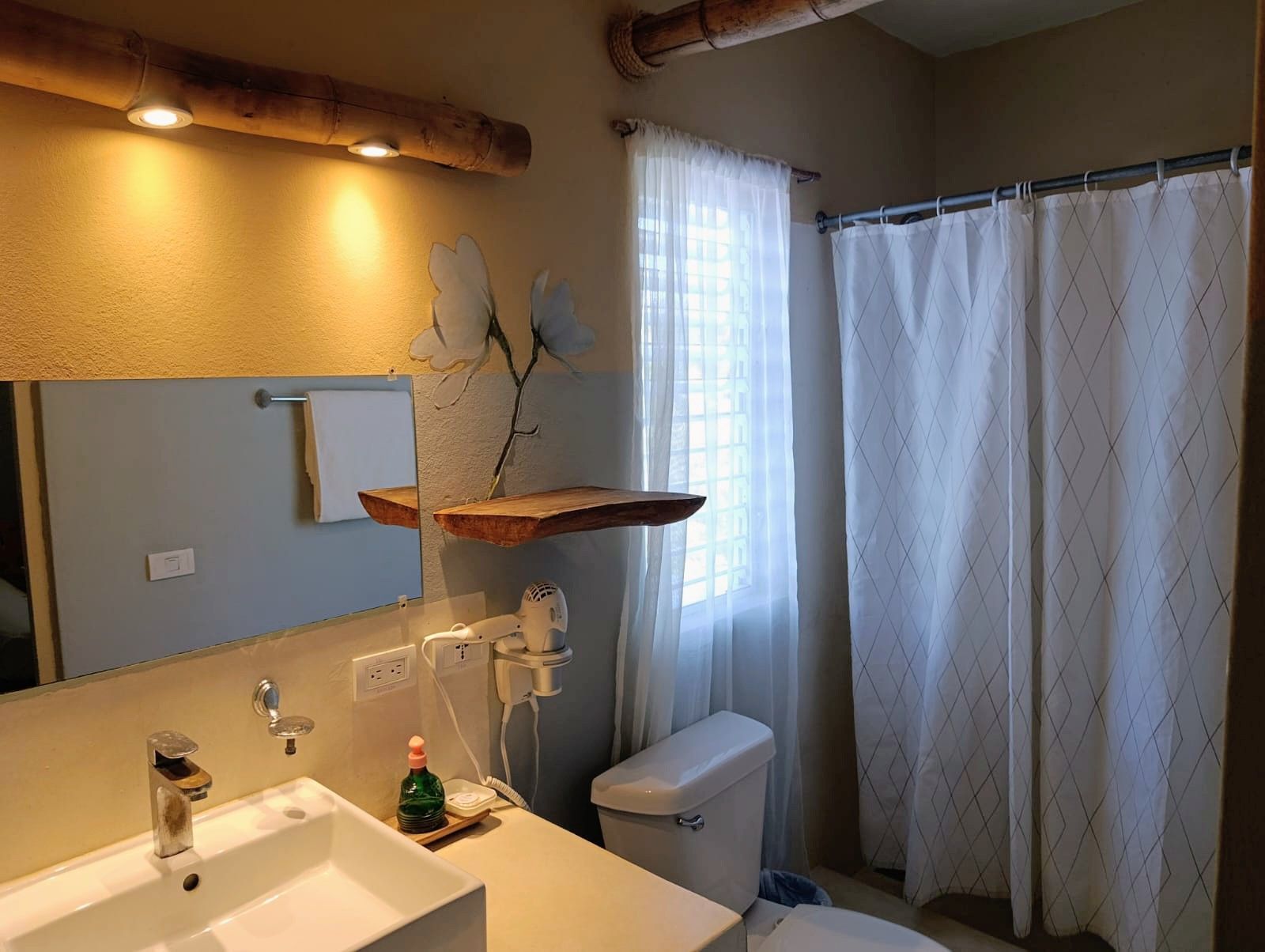 Bathroom with sink, mirror, toilet, and shower. Tan walls, bamboo accents, and a white shower curtain.