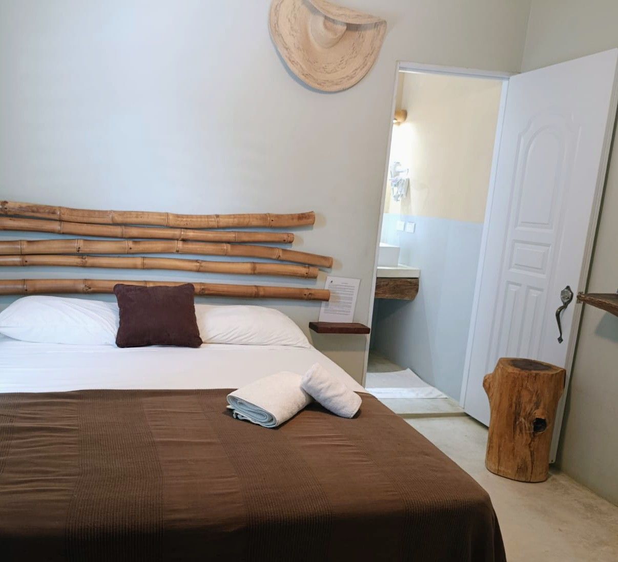 Bedroom with bamboo headboard, brown bedding, open doorway to a bathroom, and a tree stump side table.
