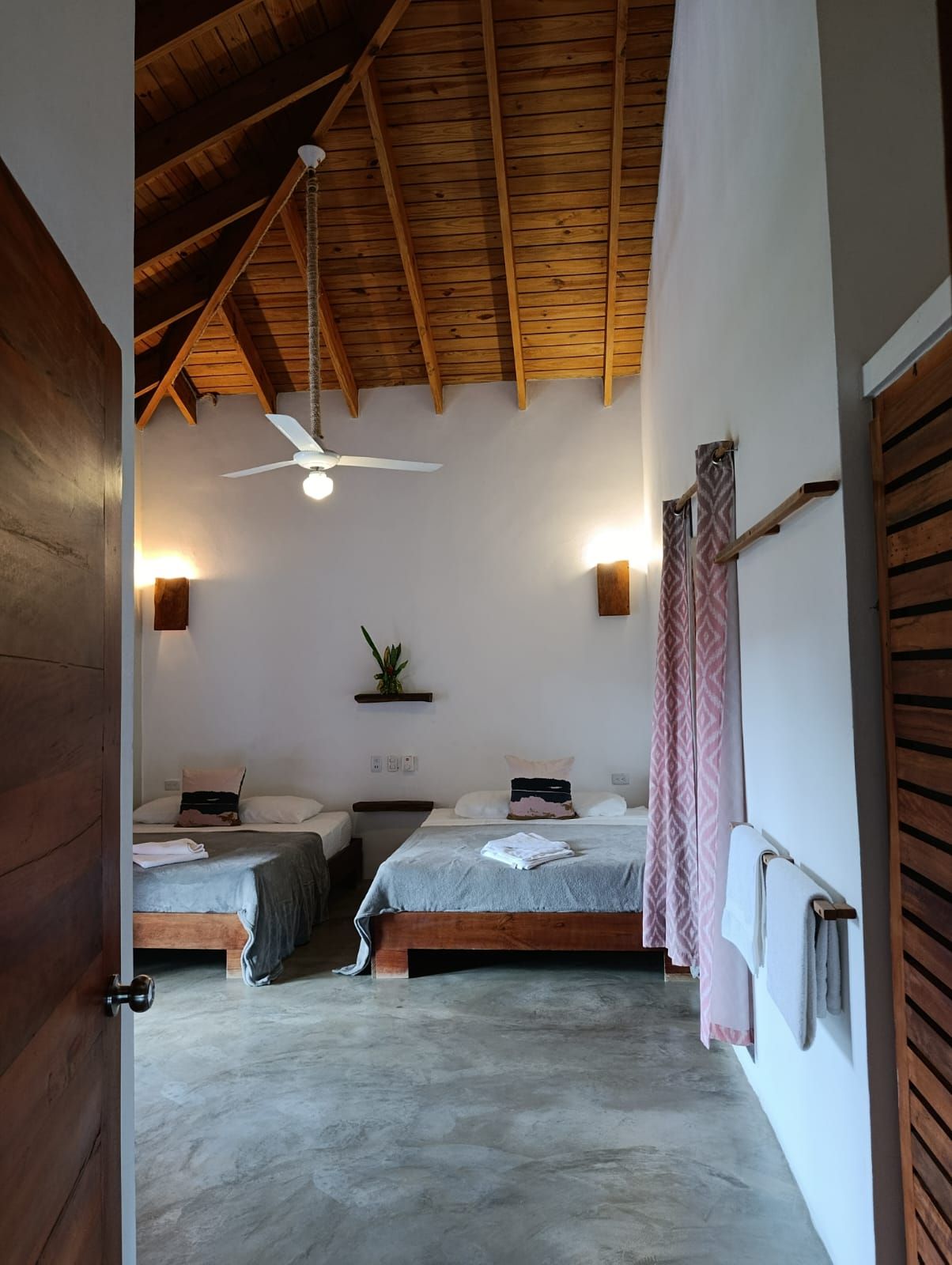 Bedroom with two beds, white walls, wood ceiling, fan, and open door.