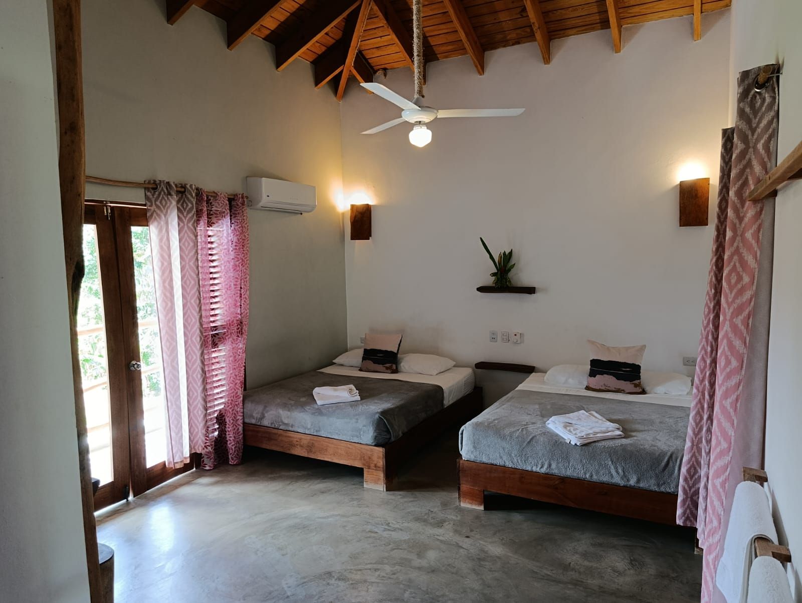 Bedroom with two twin beds, white walls, wooden ceiling, and a doorway to a balcony.