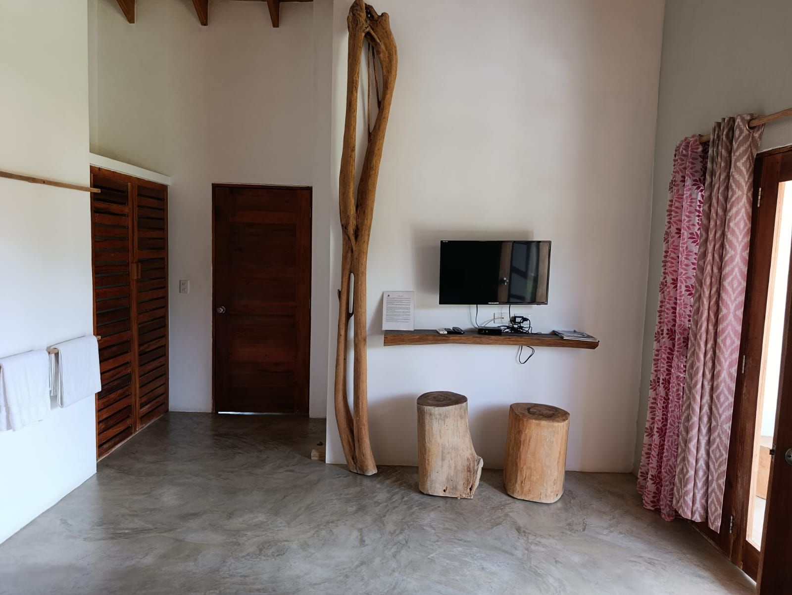 Interior with wooden door, TV, log stools, large wood sculpture, and patterned curtain.