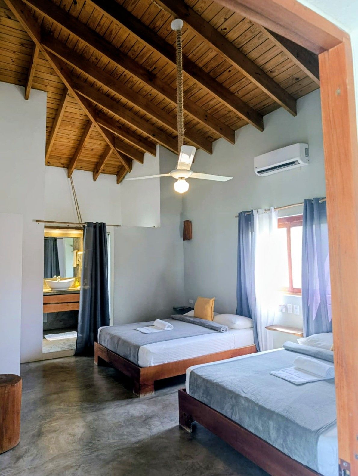 Bedroom with two beds, wooden ceiling, and bathroom door open to a sink and mirror.