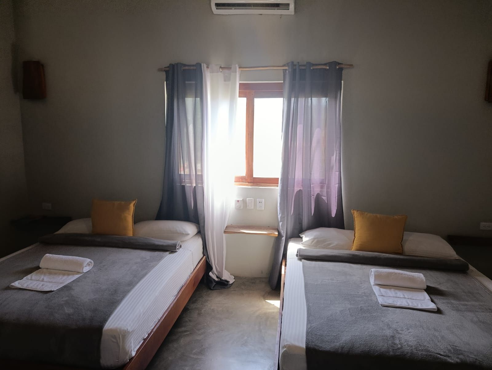 Two twin beds in a room with a window, gray and yellow bedding, gray and white curtains.