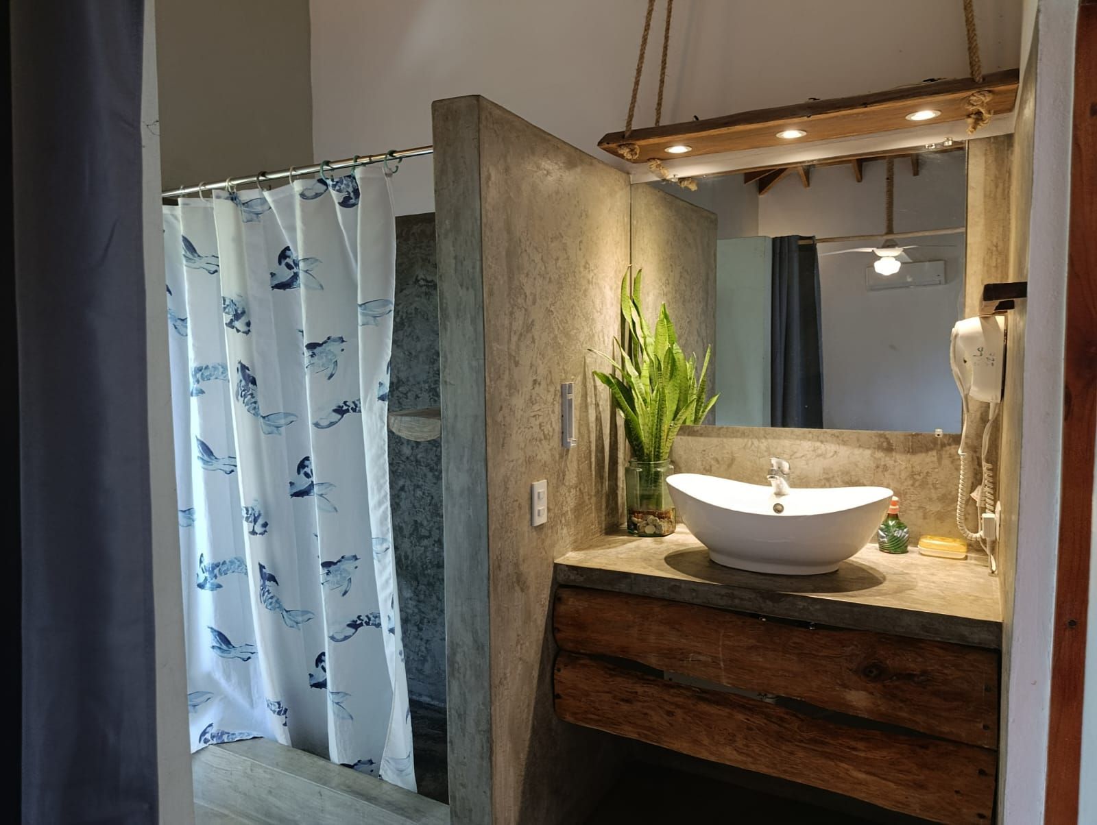 Bathroom with shower, concrete walls, white sink, wood vanity, and a rustic mirror.