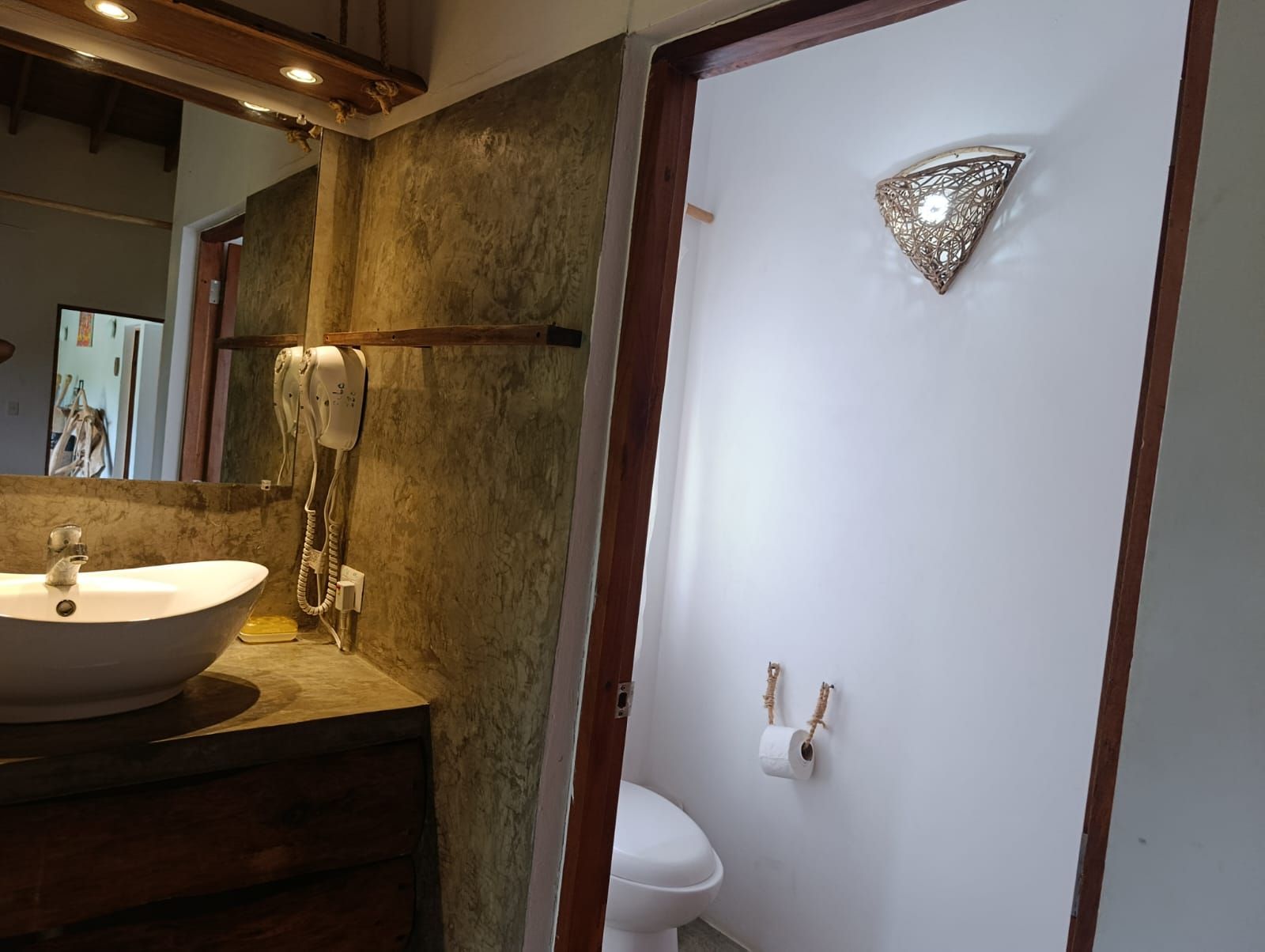 Bathroom with sink, mirror, and toilet. White walls, wood trim, and decorative light.