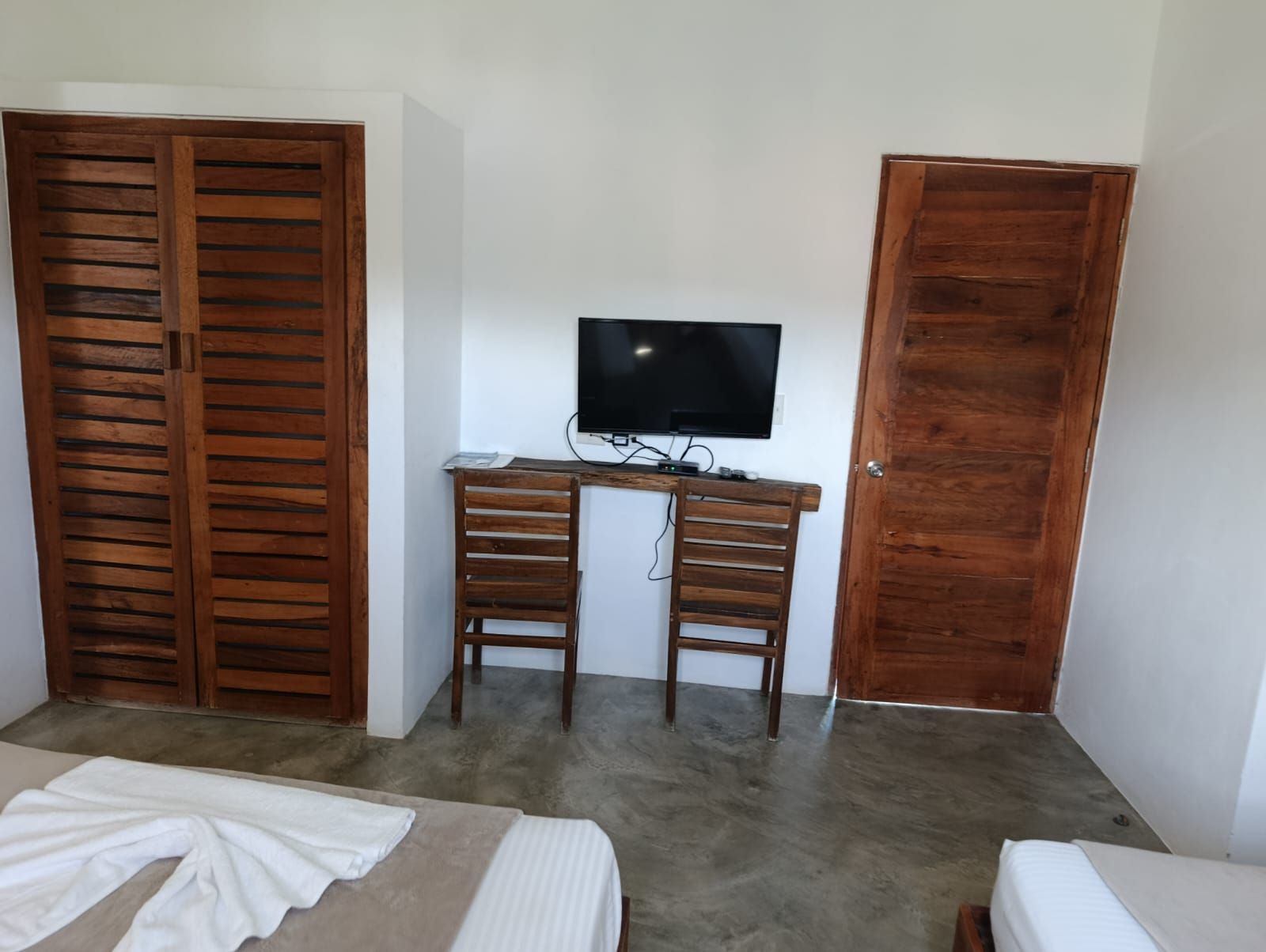 Bedroom with wooden wardrobe and door, TV on a wooden table, and beds with white linens.
