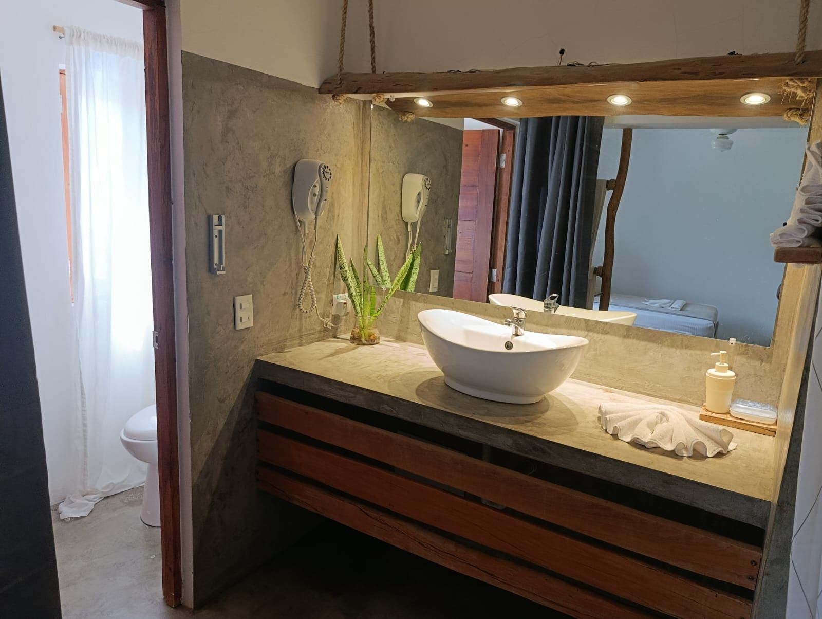 Bathroom with a white oval sink on a concrete countertop and wooden cabinet. Gray walls, large mirror, and open door.