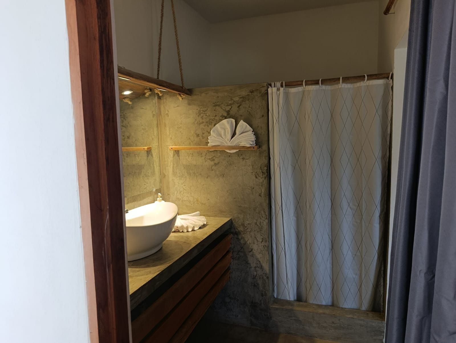 Bathroom with a gray concrete wall, white sink, wooden accents, and a shower with a white curtain.