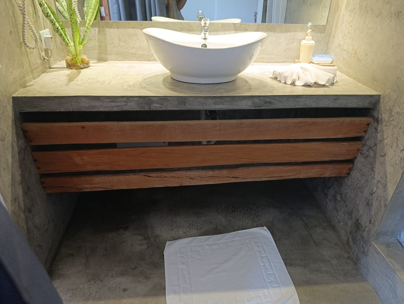Modern bathroom sink with a wooden drawer, set against a concrete wall.