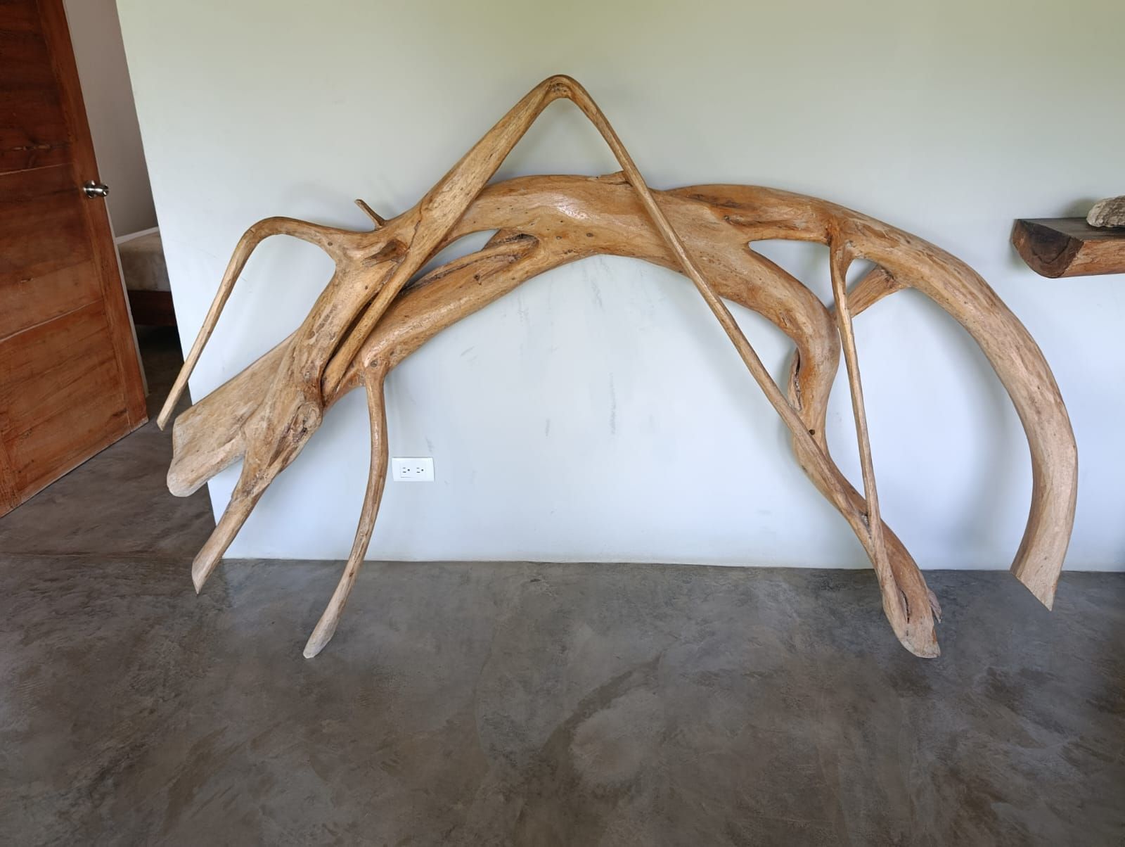 A wooden sculpture of a pterosaur on a wall, tan with outstretched wings, indoor setting.
