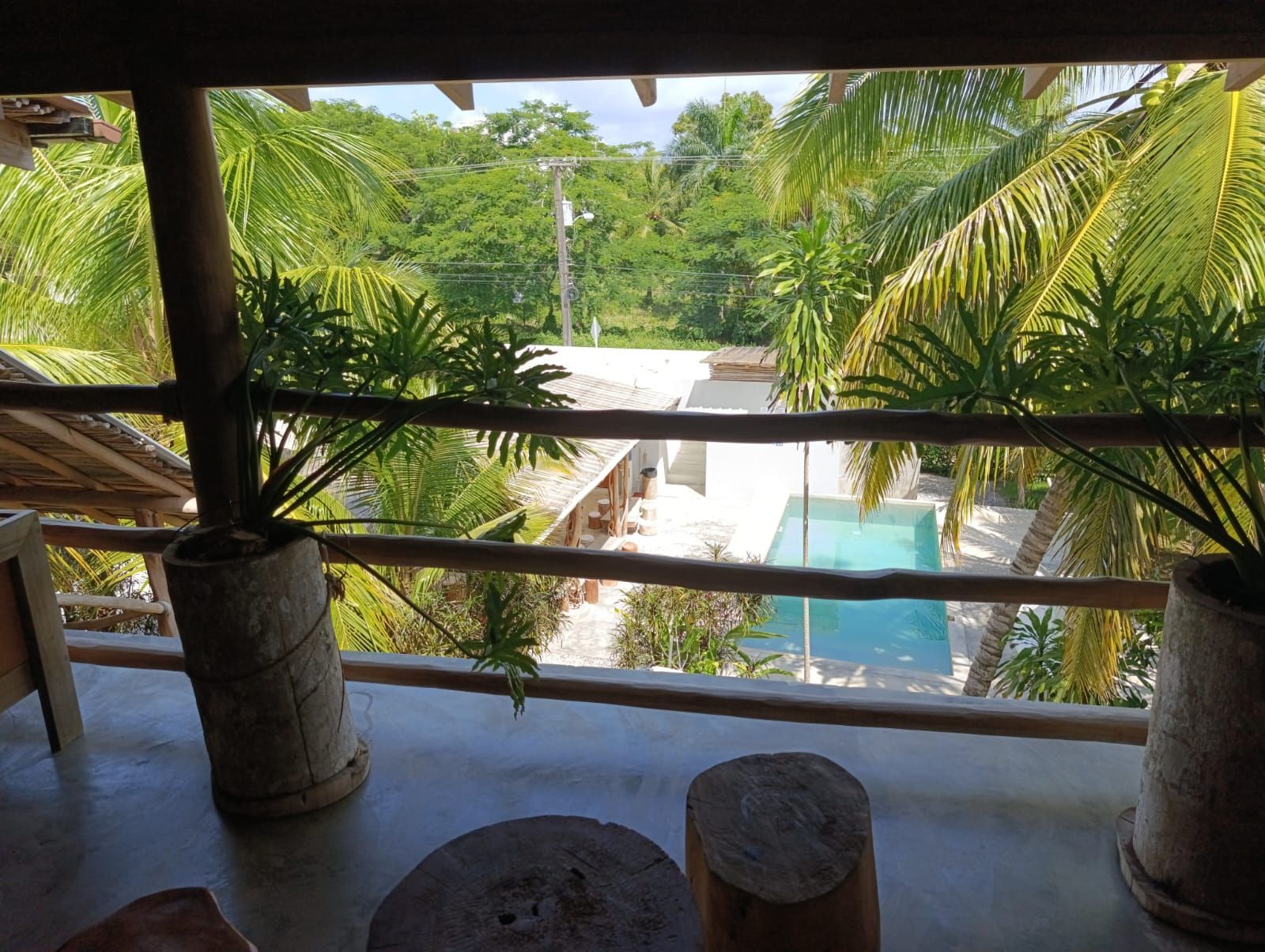 Balcony view of pool, trees, and greenery, rustic wooden railing. Sunny day.