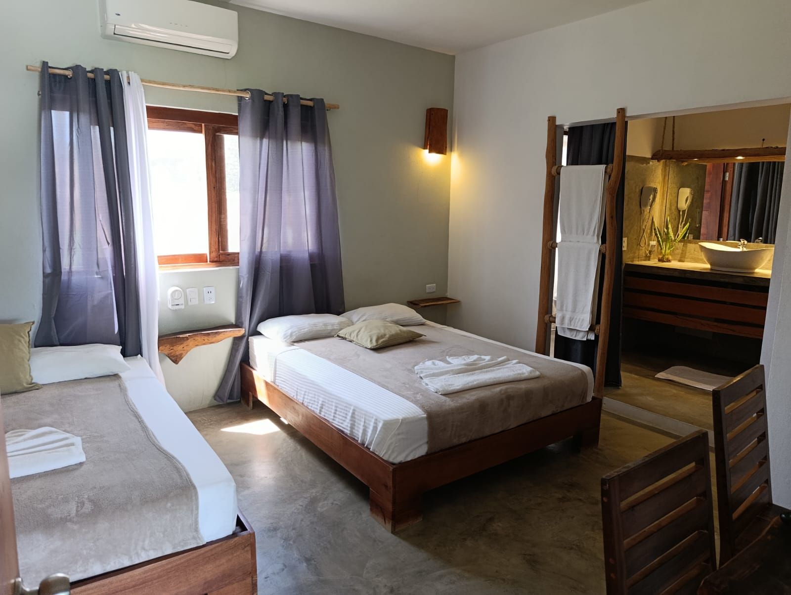 A bright hotel room with two beds, a window, and an open bathroom.