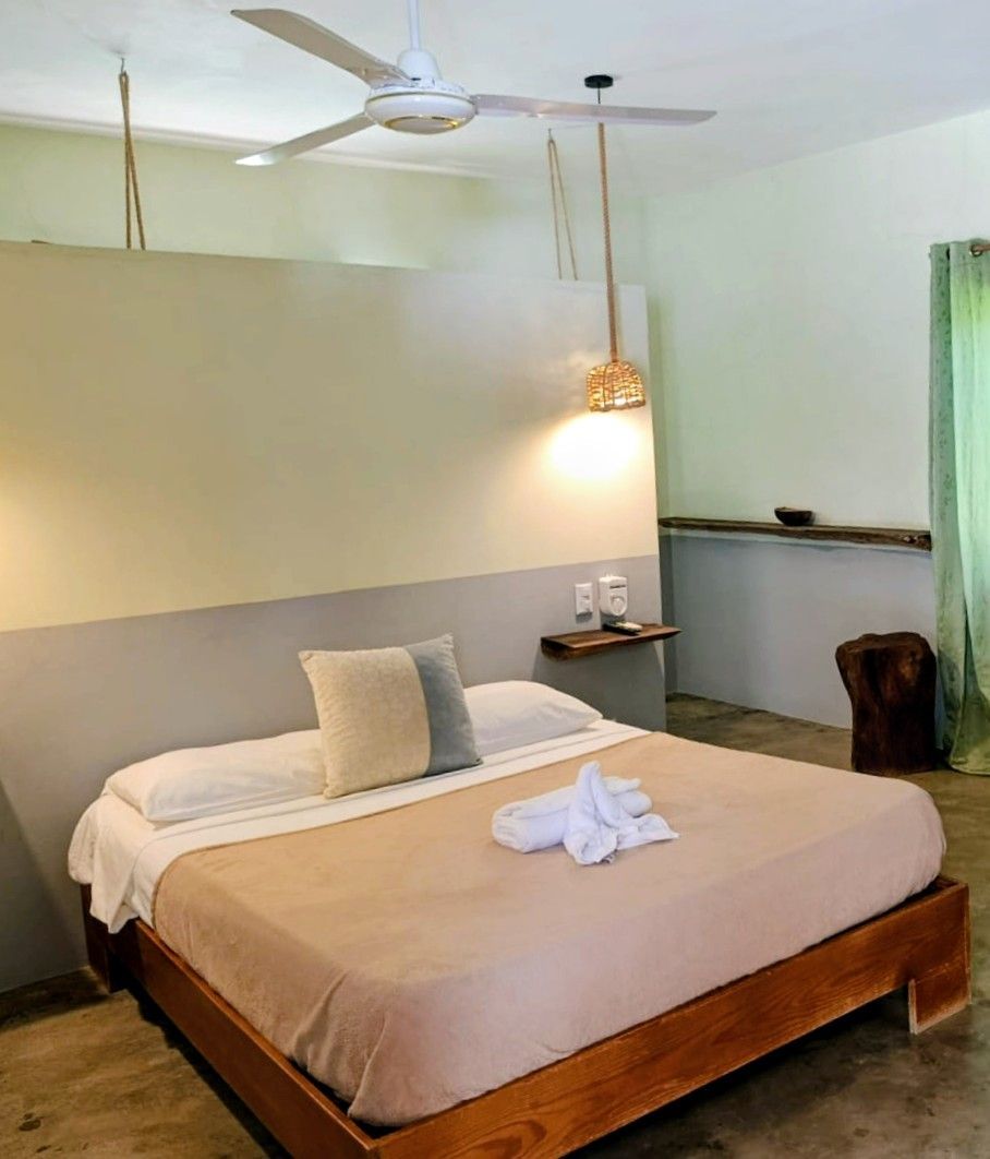 Bedroom with a large bed, neutral colors, wooden accents, and a ceiling fan.