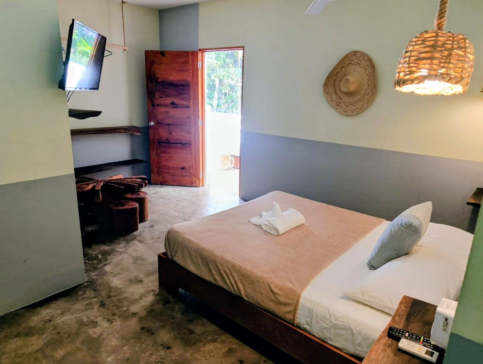 Bedroom with a bed, television, open wooden door, and decorative woven pendant lamp.
