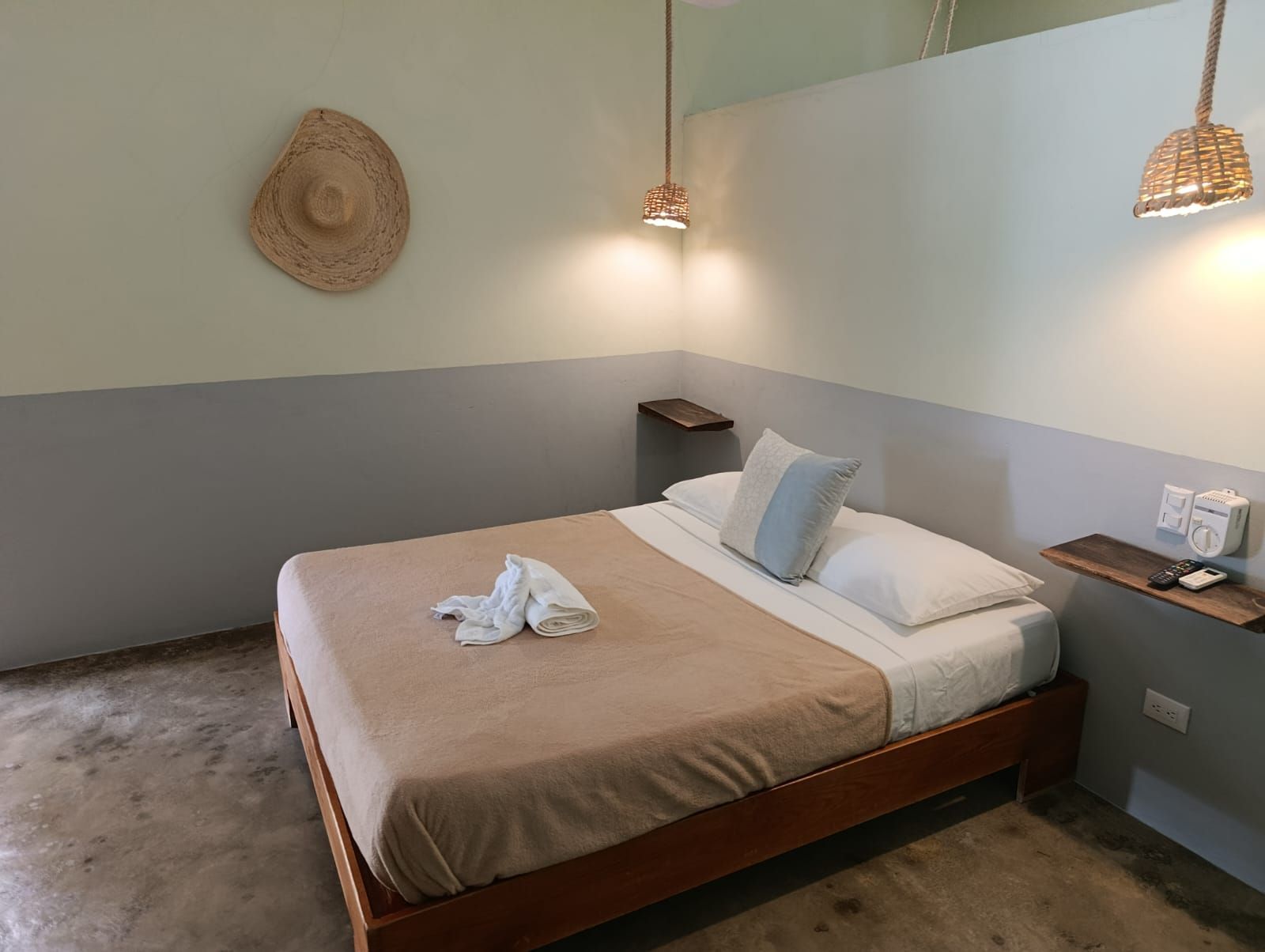 Bedroom with bed, bedside tables, two-tone walls (gray, light green), woven lamp shades, and decorative straw hat.