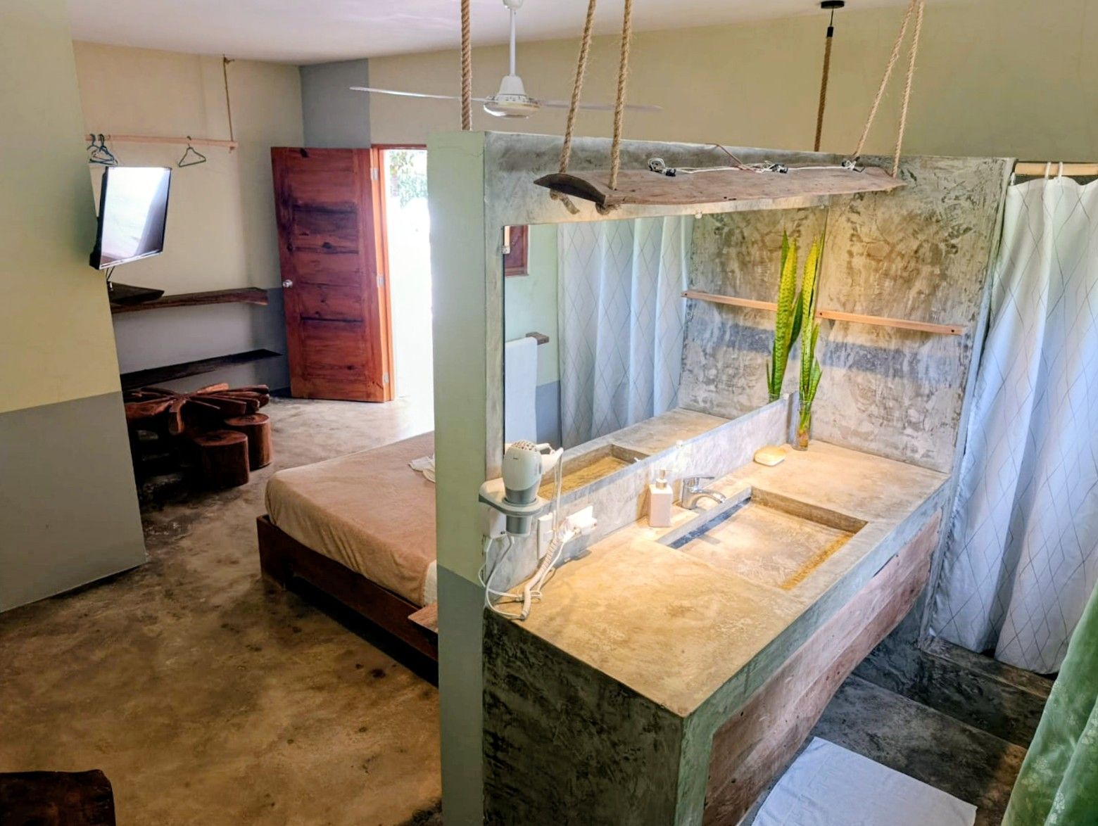 Open-concept room with a bed, a concrete vanity, and a wooden door leading outside.