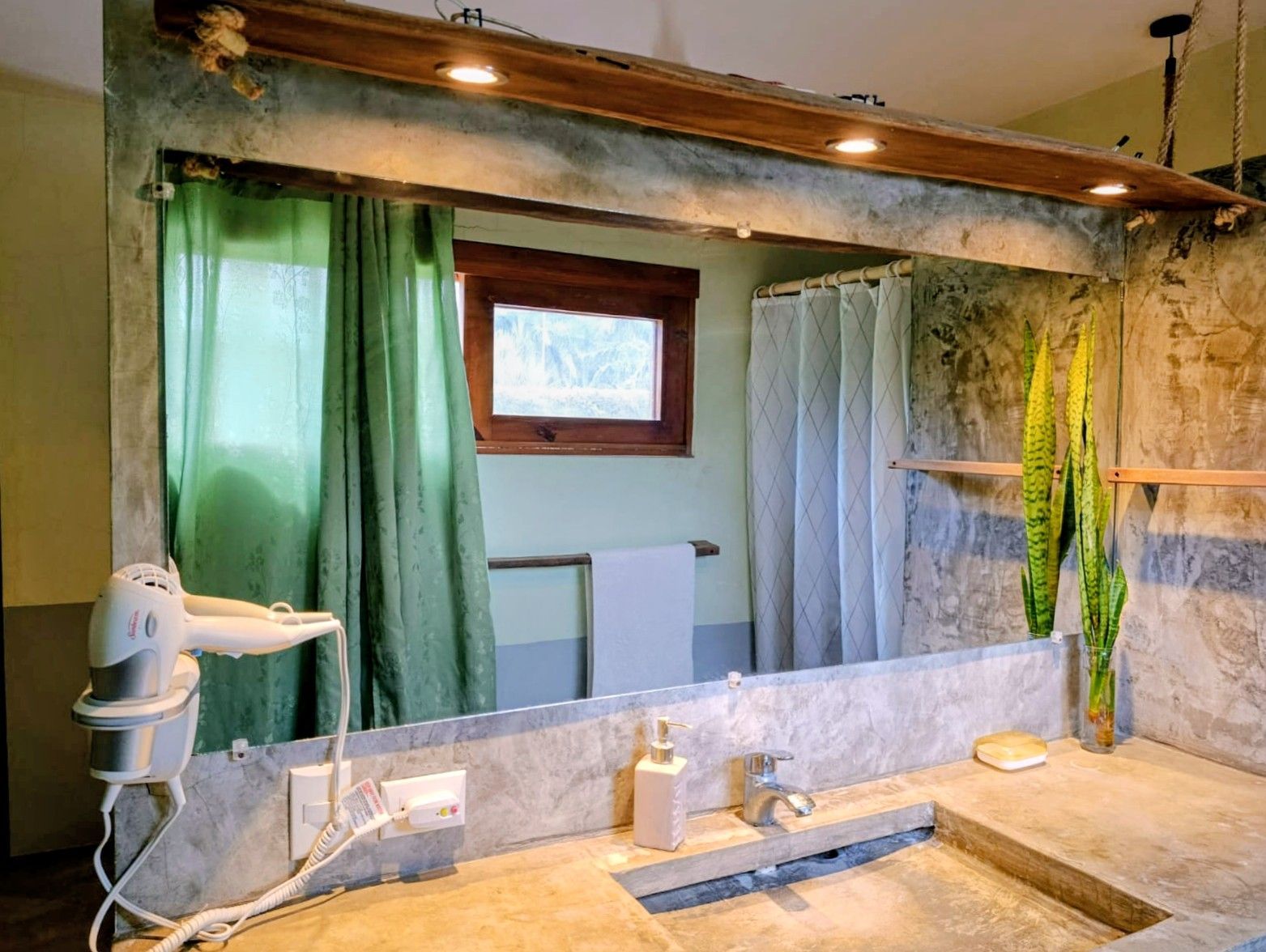 Bathroom with concrete walls, large mirror, wooden accents, and a window.