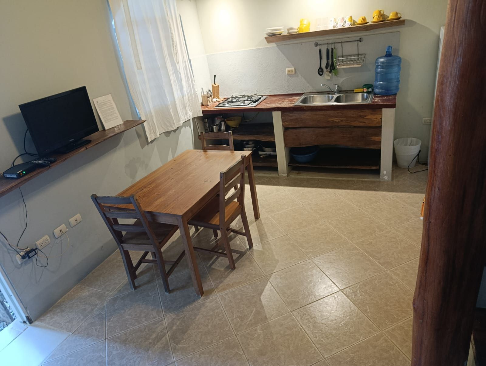 A small kitchen with a wooden table and chairs, a sink, and a television.