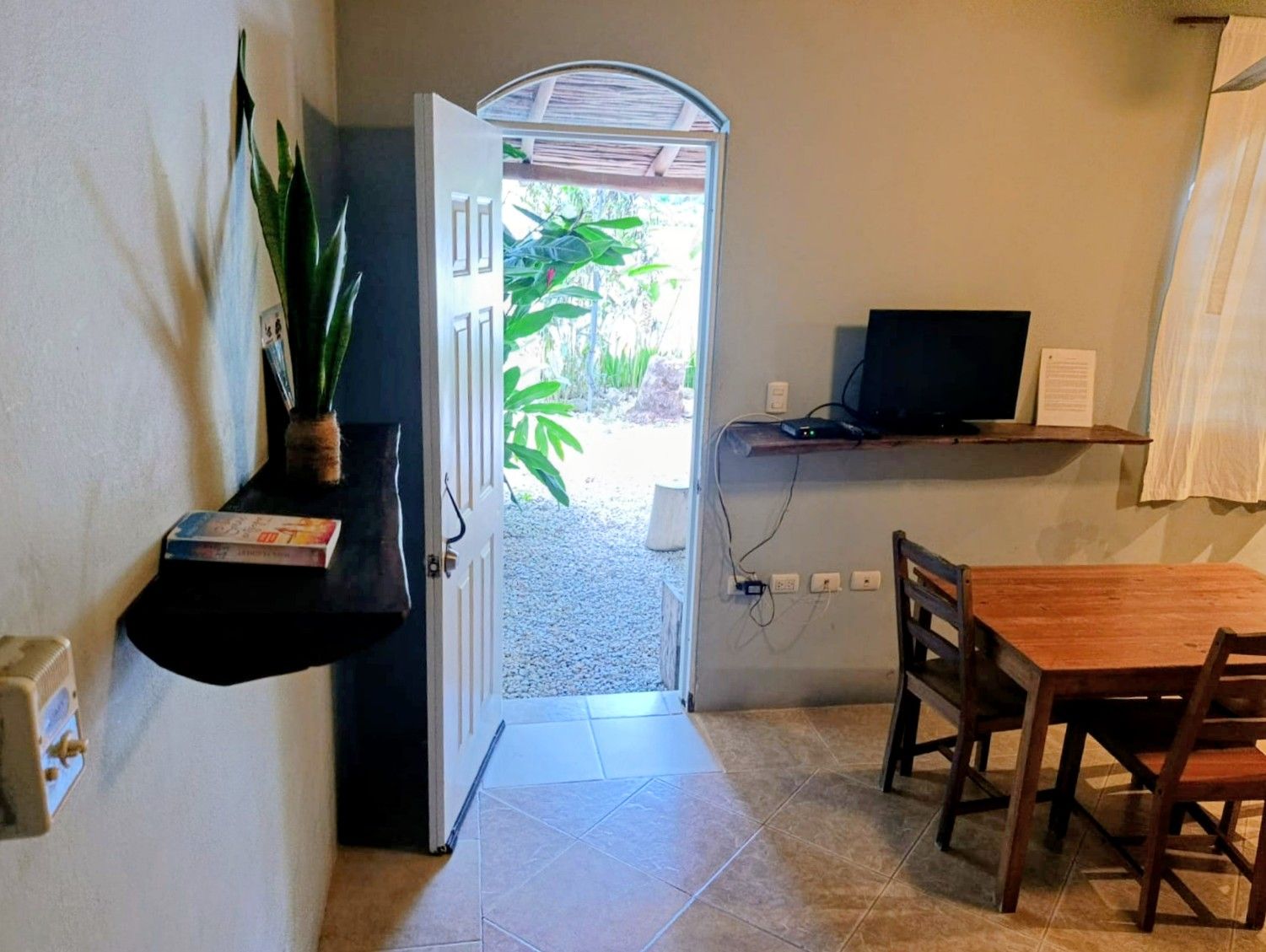 Interior room with open door to garden, small dining area, and wall-mounted TV.
